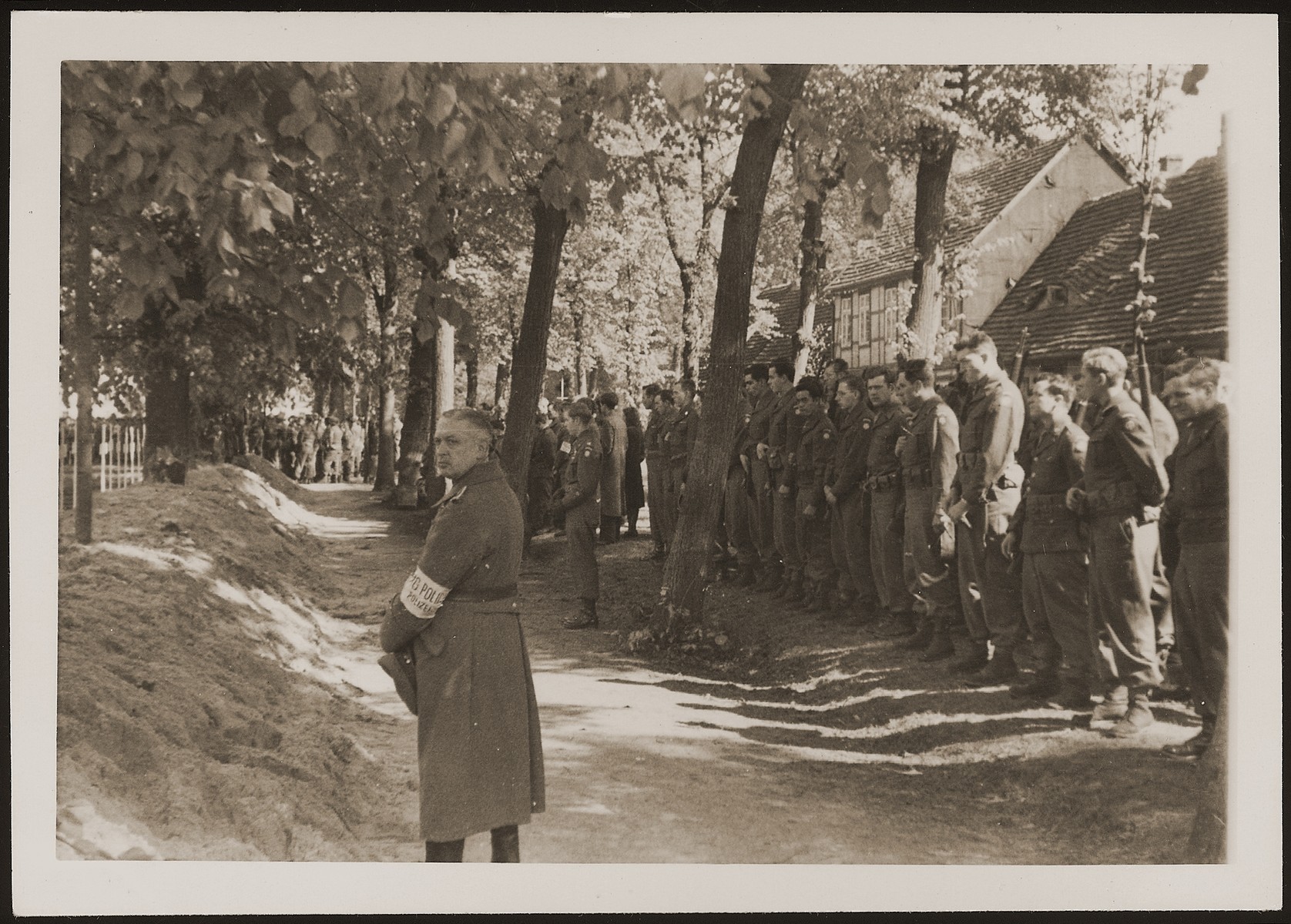 American soldiers and a German policeman observe a moment of silence at a mass funeral on the palace grounds of the Archduke of Mecklenburg, where the townspeople were forced by U.S. troops to bury the corpses of prisoners killed in the Woebbelin concentration camp .