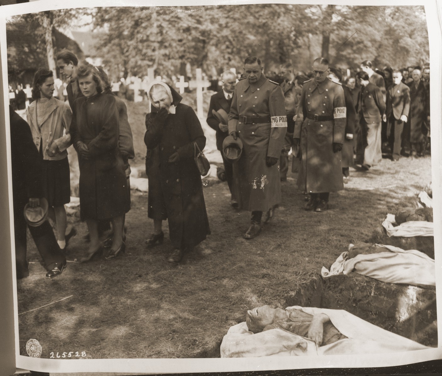 Civilians of all ages are forced to march past the open graves of victims from the concentration camp at Woebbelin.  The townspeople were forced by U.S. troops to bury the corpses on the palace grounds of the Archduke of Mecklenburg.