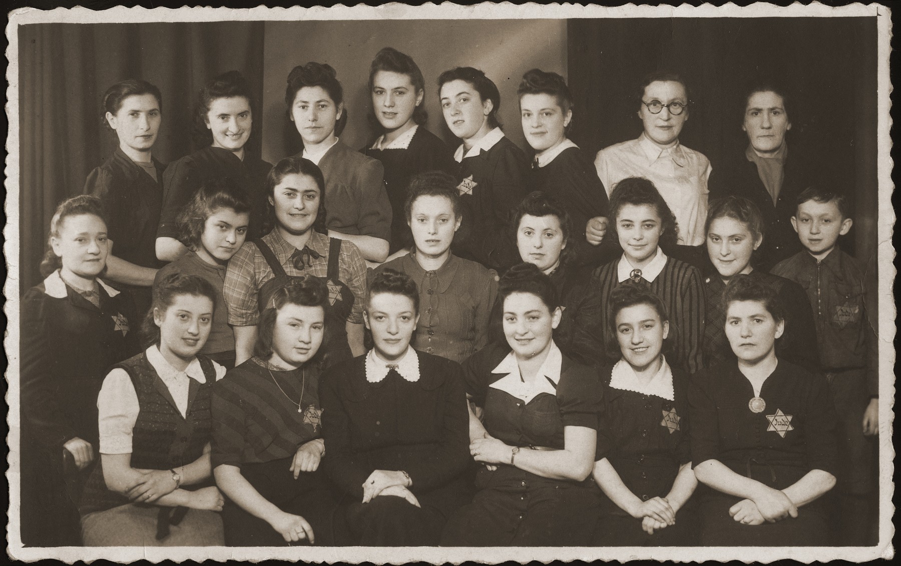 Group portrait of young women wearing Jewish badges, who worked in a sewing workshop in Bedzin.  

The donor, Ruzia Grinbaum is pictured in the front row, third from the right.  The little boy, standing in the middle row at the far right, was hidden in the workshop by his mother, who is seated directly in front of him.  Of the entire group, only the donor survived the war.