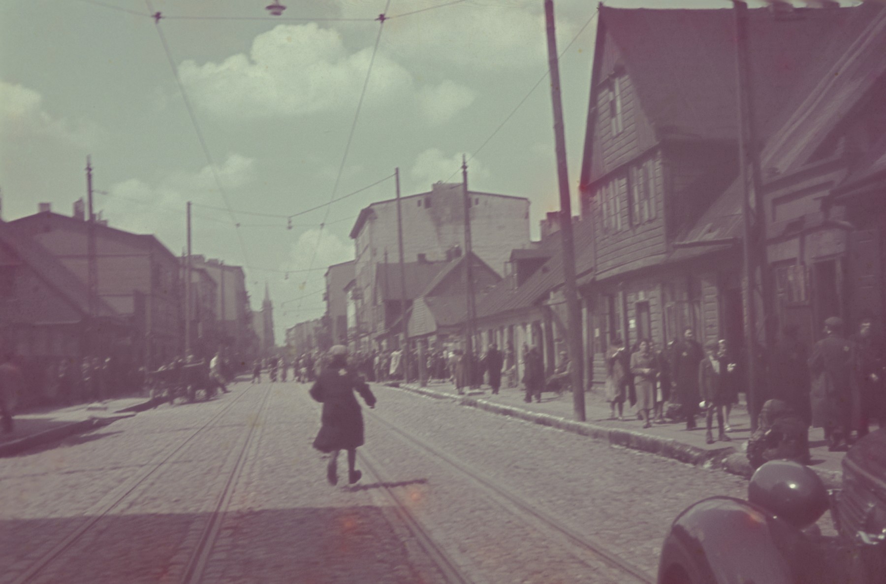 A Jewish man runs down street in the Lodz ghetto in front of an automobile.