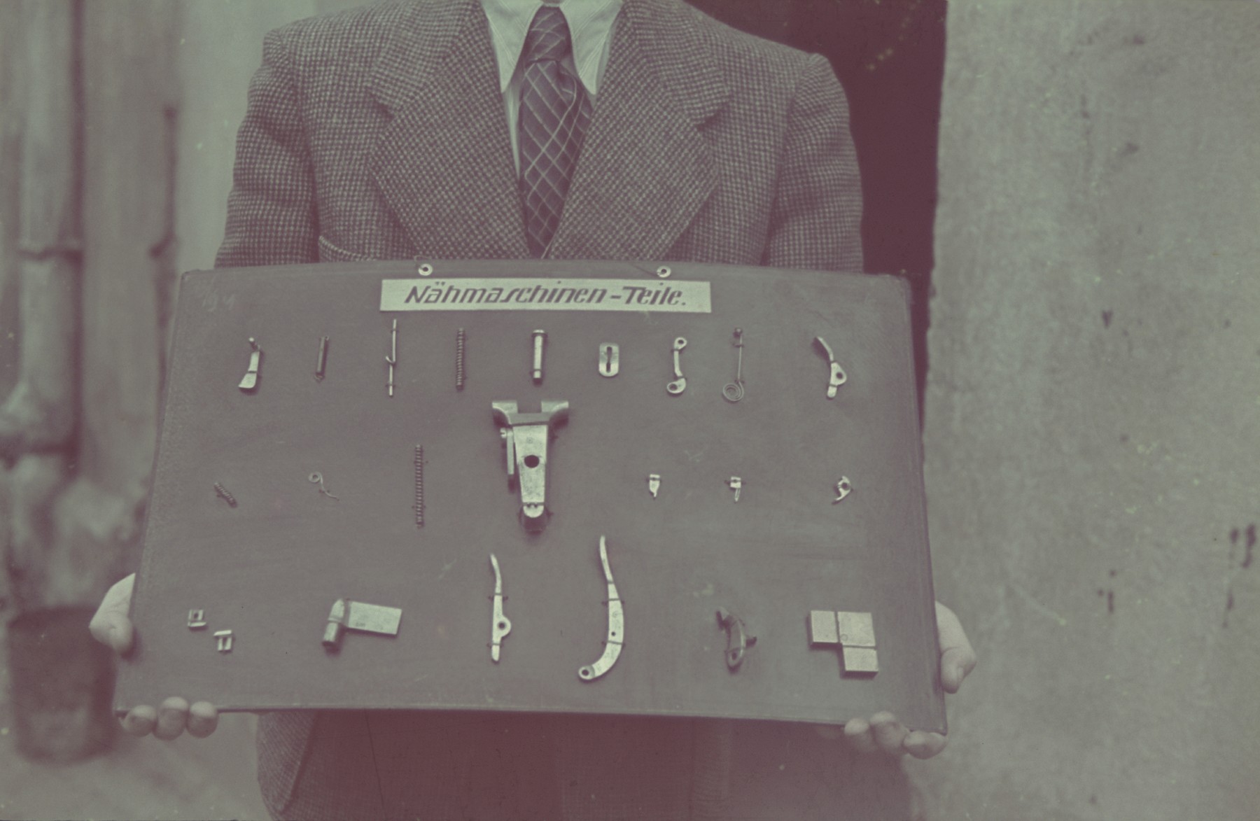 A man holds a display of sewing machine parts in the Lodz ghetto.

Original German caption: "Getto Litzmanndstadt, Aus der Feinmechanik (fine mechanics), #18.
