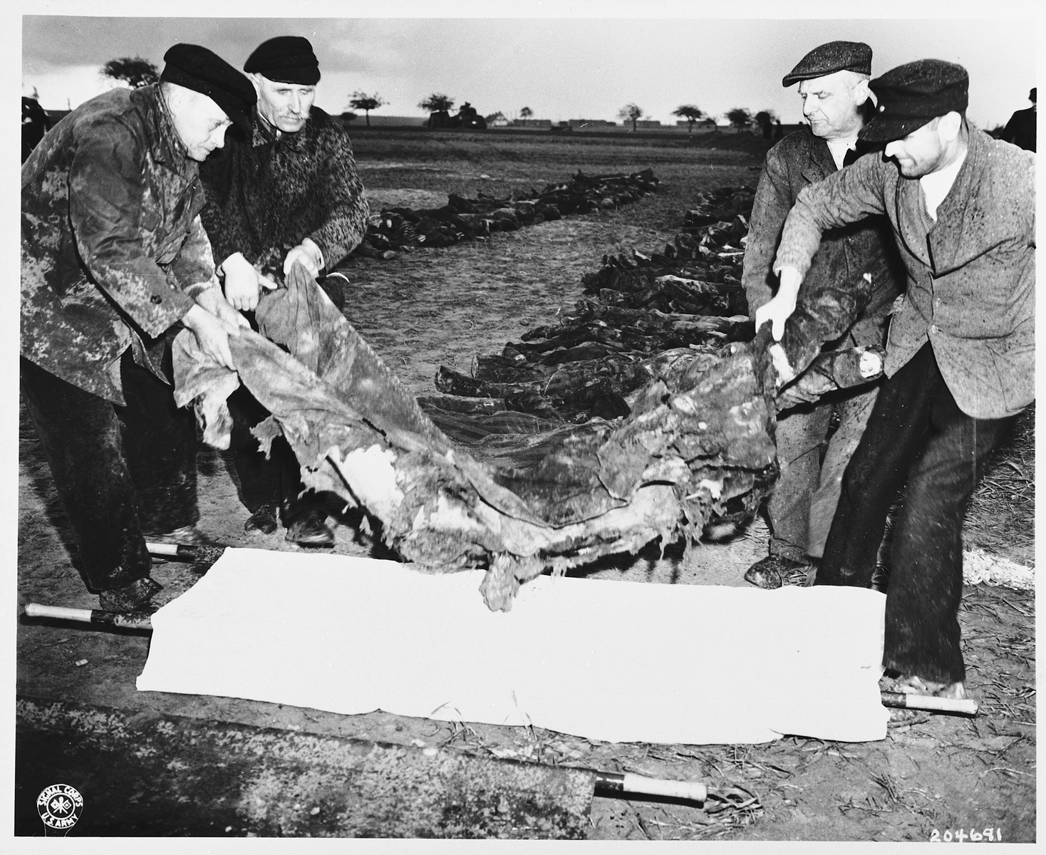German civilians transfer a corpse to a stretcher to carry to a grave.  The victim was a concentration camp prisoner who was killed by the SS in a barn just outside Gardelegen.