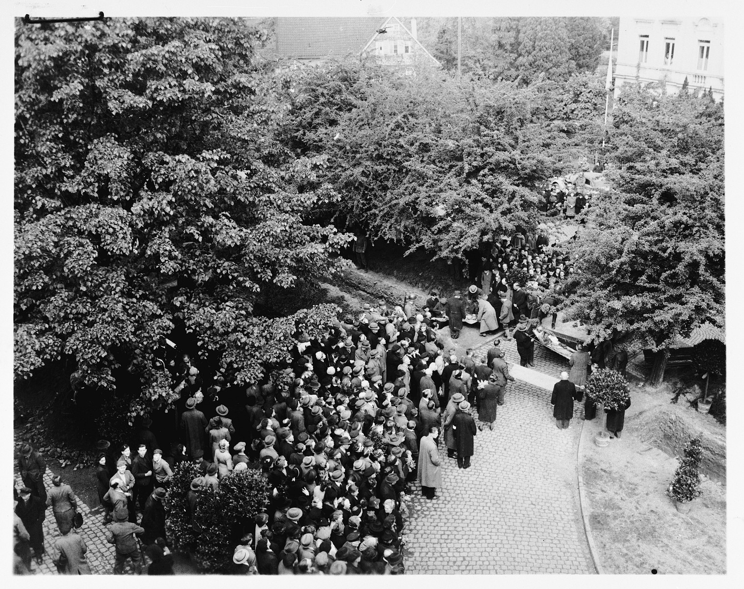 Under the direction of American soldiers, German civilians bury the bodies of 71 political prisoners, exhumed from a mass grave near Solingen-Ohligs, in new graves in front of the city hall.  

The victims, most of whom were taken from Luettringhausen prison, were shot and buried by the Gestapo following orders to eliminate all Reich enemies just before the end of the war.
