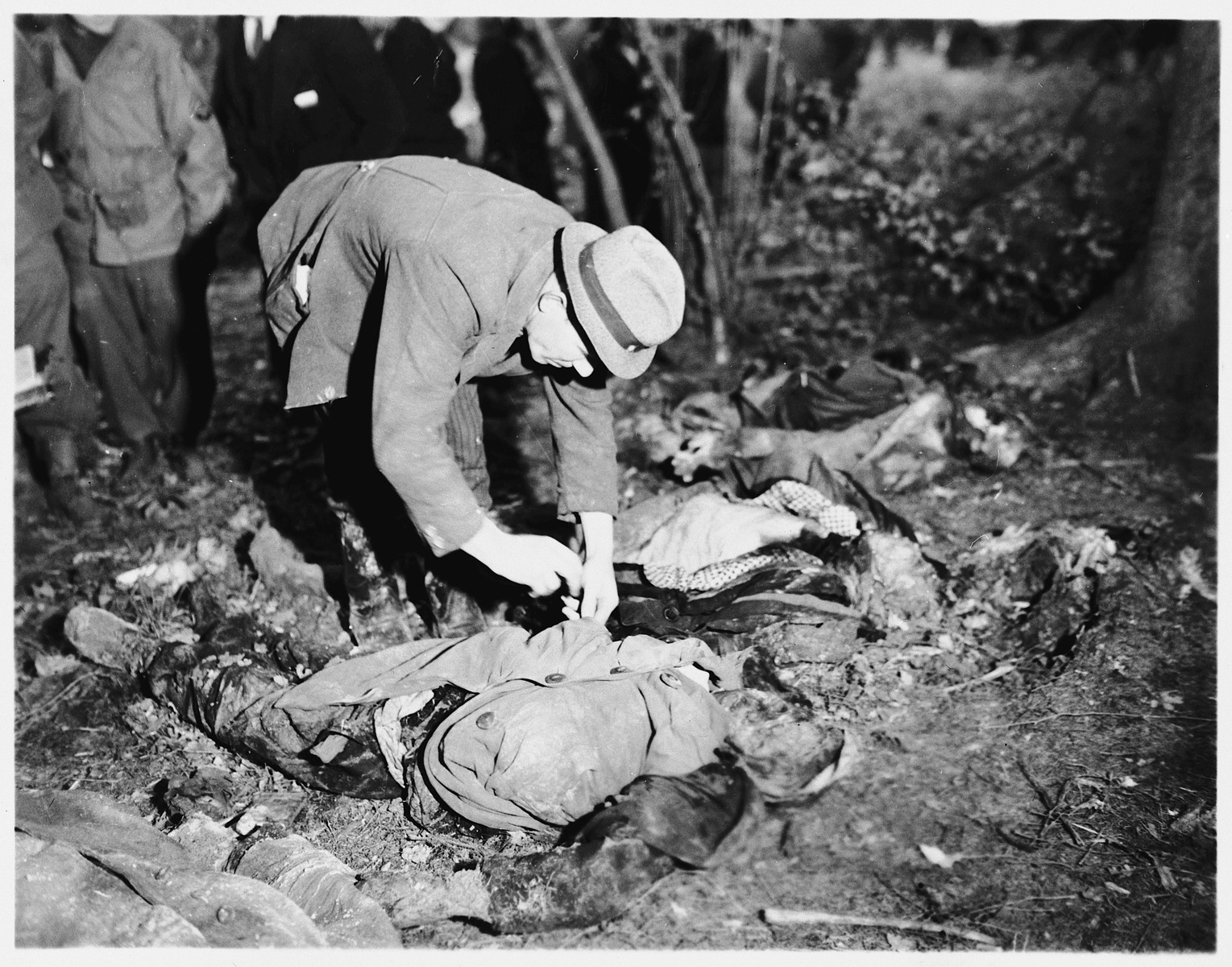 A man looks for identification papers on one of the 57 corpses of Russians, including women and one baby, exhumed from a mass grave near Suttrop.  

The victims were forced to dig their own grave and then were shot by SS troops six weeks before the arrival of American troops.  On May 3, 1945, the 95th Infantry Division of the U.S. Ninth Army arrived in Suttrop and were informed by locals of the mass grave.  American troops forced the townspeople to exhume the grave after which Russian displaced persons in the area identified the bodies.  The victims were reburied in individual graves, and a U.S. Army chaplain conducted burial services.  Russians remaining in the area placed wreaths on the graves.