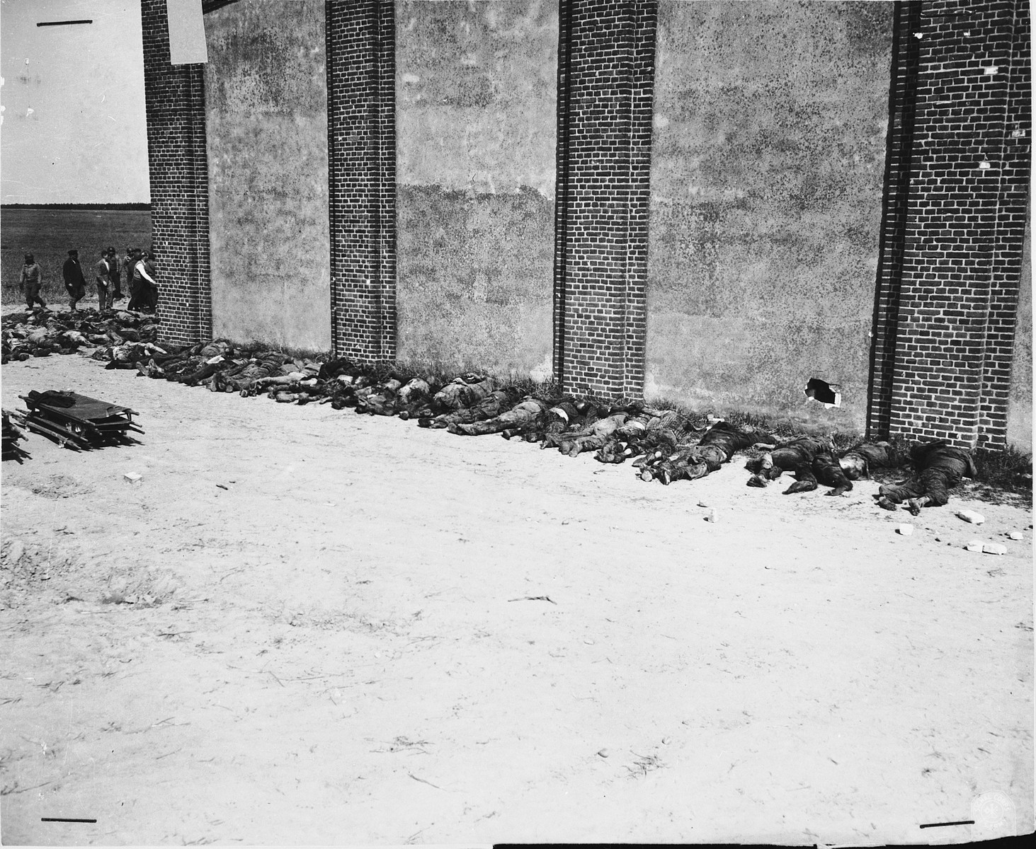 Corpses lined up on the west side of the barn with a visible hole supposedly made by a Panzerfaust.  In the background German civilians remove corpses from the barn.