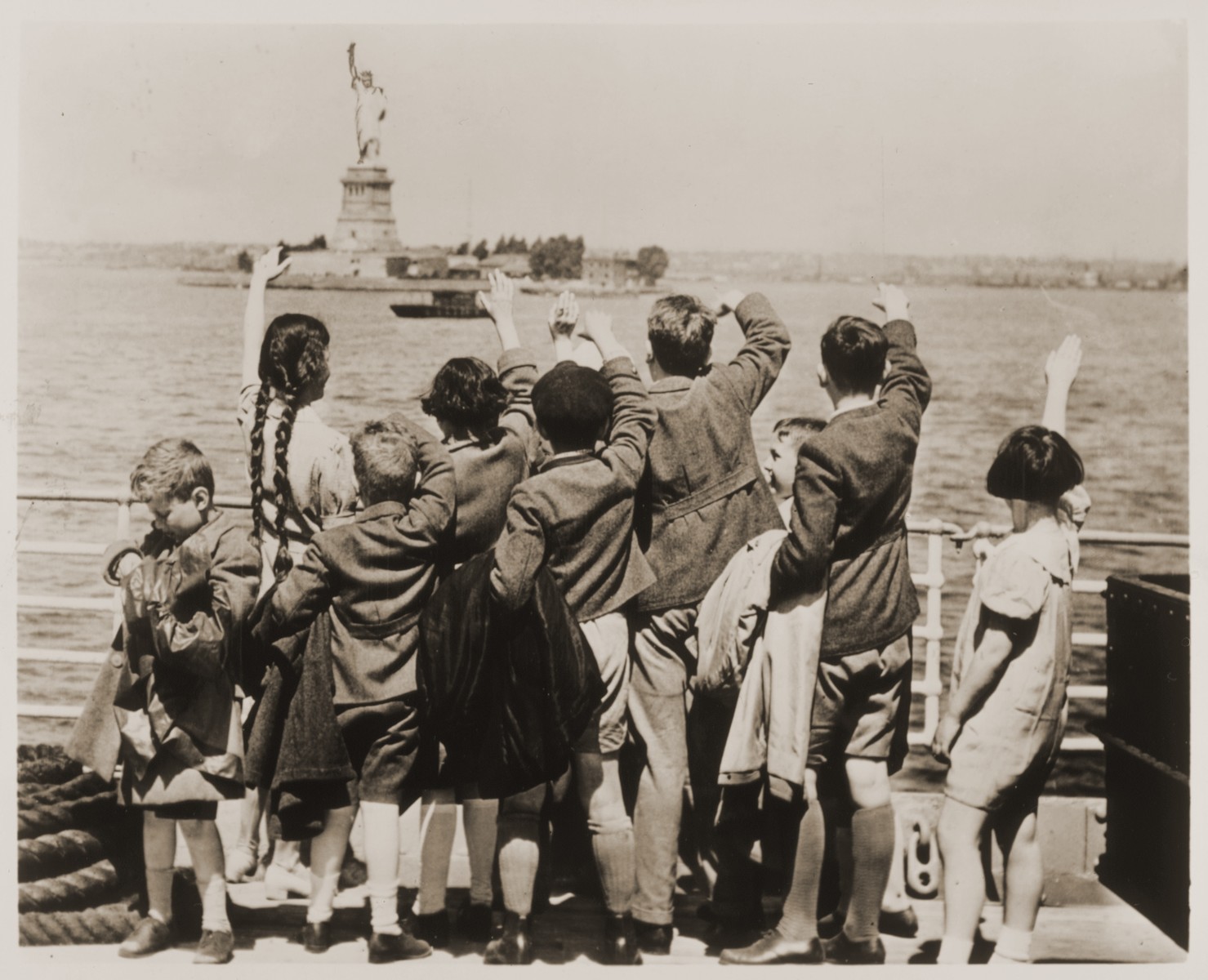 Jewish refugee children wave at the Statue of Liberty as the President Harding steams into New York harbor.

These children are among a group of fifty Jewish refugees (25 boys and 25 girls) from Vienna, aged 5 to 14, who are en route to Philadelphia, where they will be placed with foster families.  The children were accompanied by Gilbert J. Kraus, a Philadelphia attorney, and his wife Eleanor, who had worked for months to secure their admission into the U.S.

Among those pictured is Johanna Braun Gitlin (two, long braids).