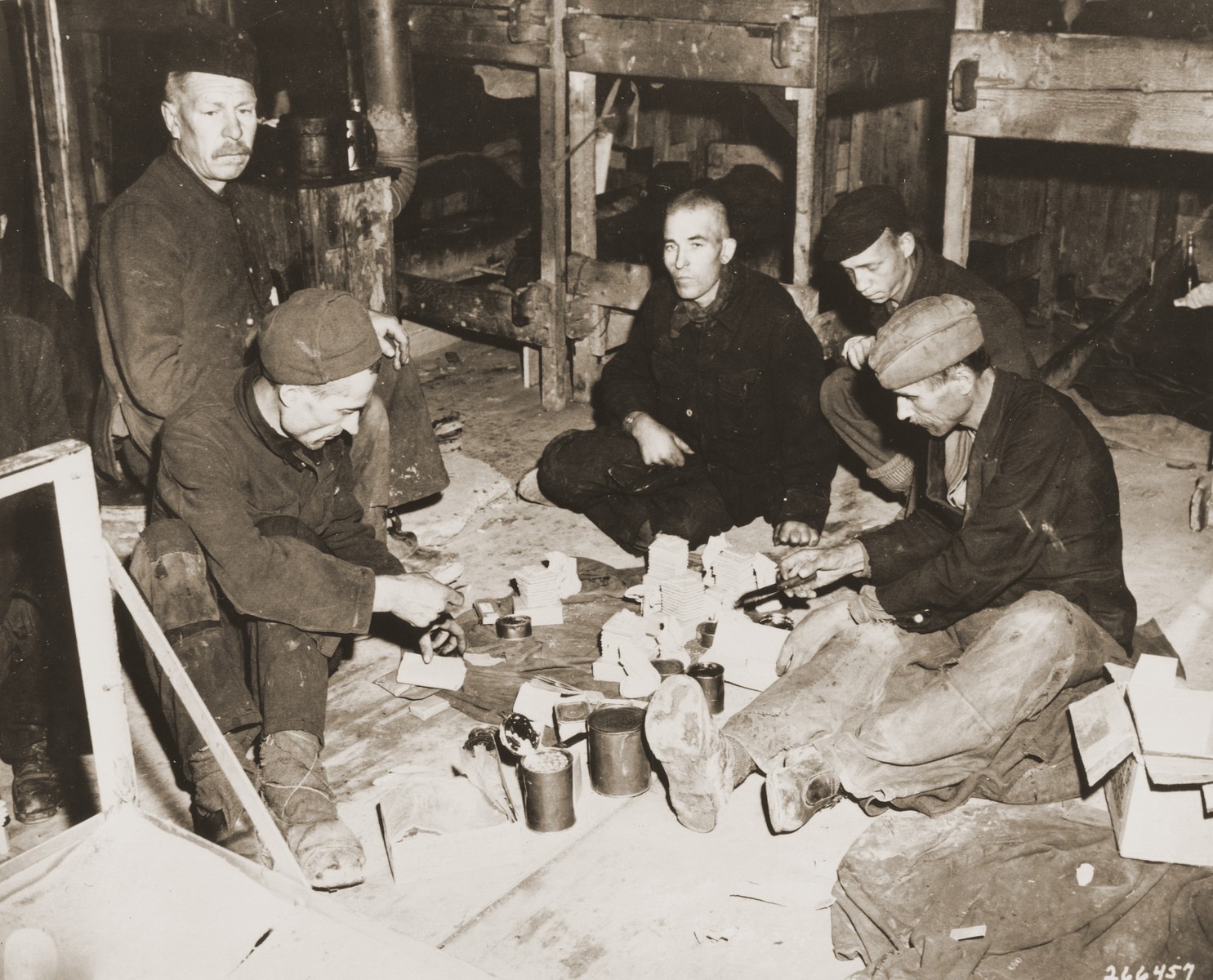 A group of Soviet POWs share rations in the newly liberated Hemer POW camp.

Original caption: "These gaunt-faced Soviets share a 10-in-1 ration supply kit furnished by men of a unit of the 75th Infantry Division, U.S. Ninth Army.  Soviet doctors at the camp say many of the inmates will die from malnutrition, tuberculosis, dysentery, and typhus.  Approximately 22,000 men were in the camp when it was liberated by the U.S. Army."