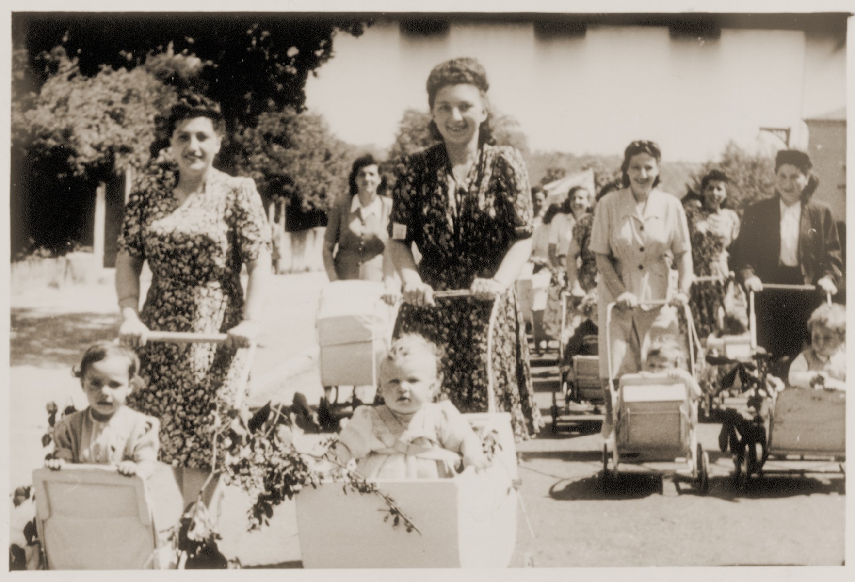 Young mothers take their babies for a stroll in the Landsberg DP camp.  

Dorit Mandelbaum is pictured in the baby carriage on the left.  Her mother, Anka, is pushing the carriage.  Chava Oppenheim pushes her son Aviezer in the carriage, third from the right.  Also pictured is Laja Minc.
