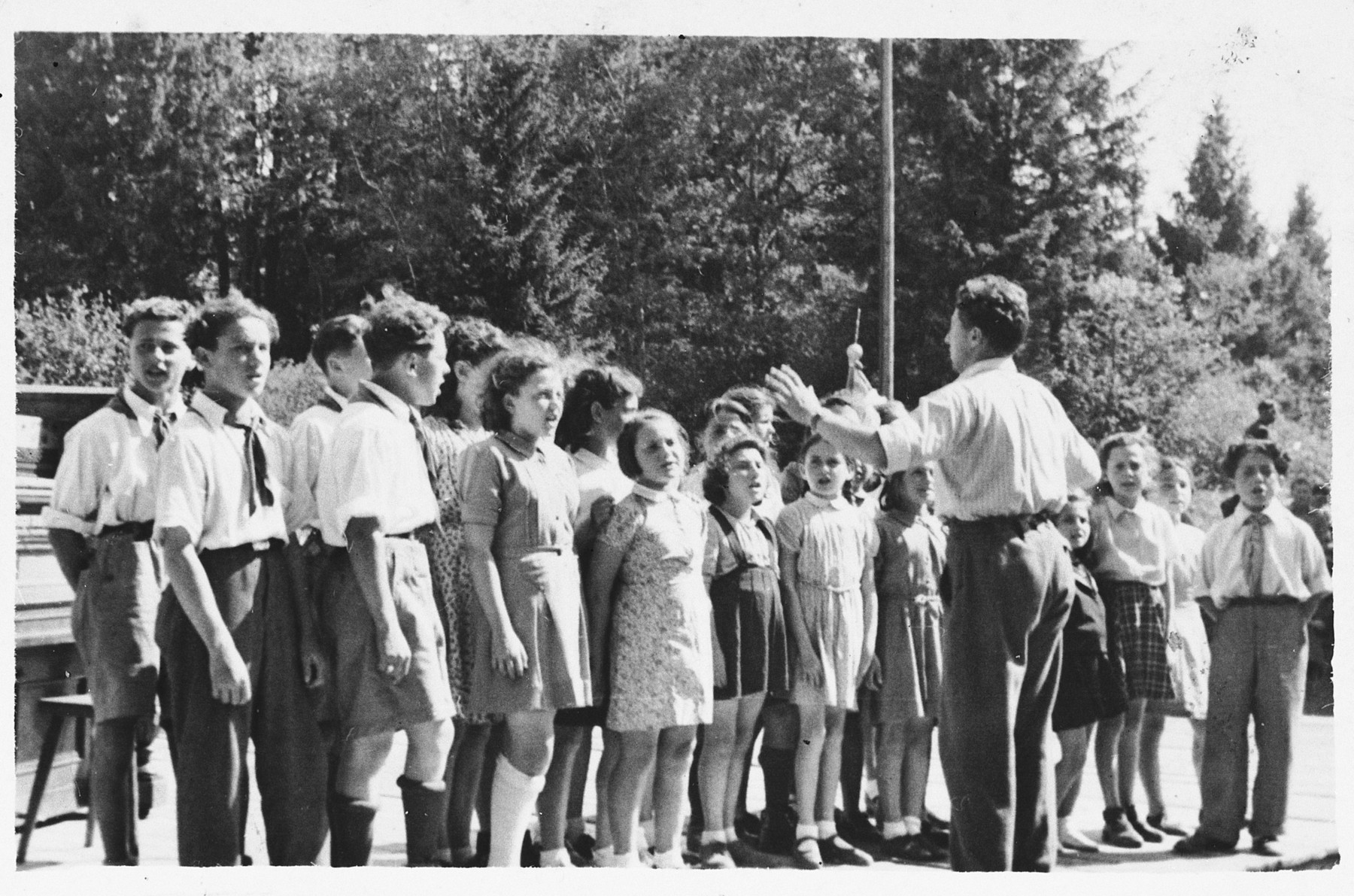 Children sing in a Lag BaOmer celebration at the Foehrenwald displaced persons camp.

Leading the singing is Stanley (Shlomo) Zektzer.