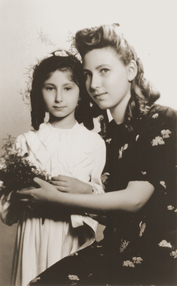 Two Jewish sisters who are living in hiding in Warsaw, pose for a formal portrait at the time of the younger girl's First Communion.

Pictured are Alicja Fajnsztejn (right) and Zofja Fajnsztejn (left).