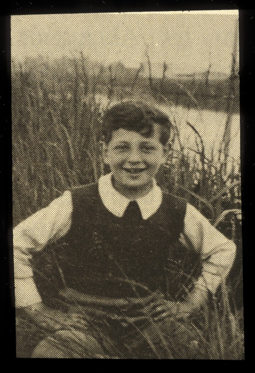 Close-up portrait of a rescued child, Nathan Zygrajcz, sitting in the tall grass by a river.