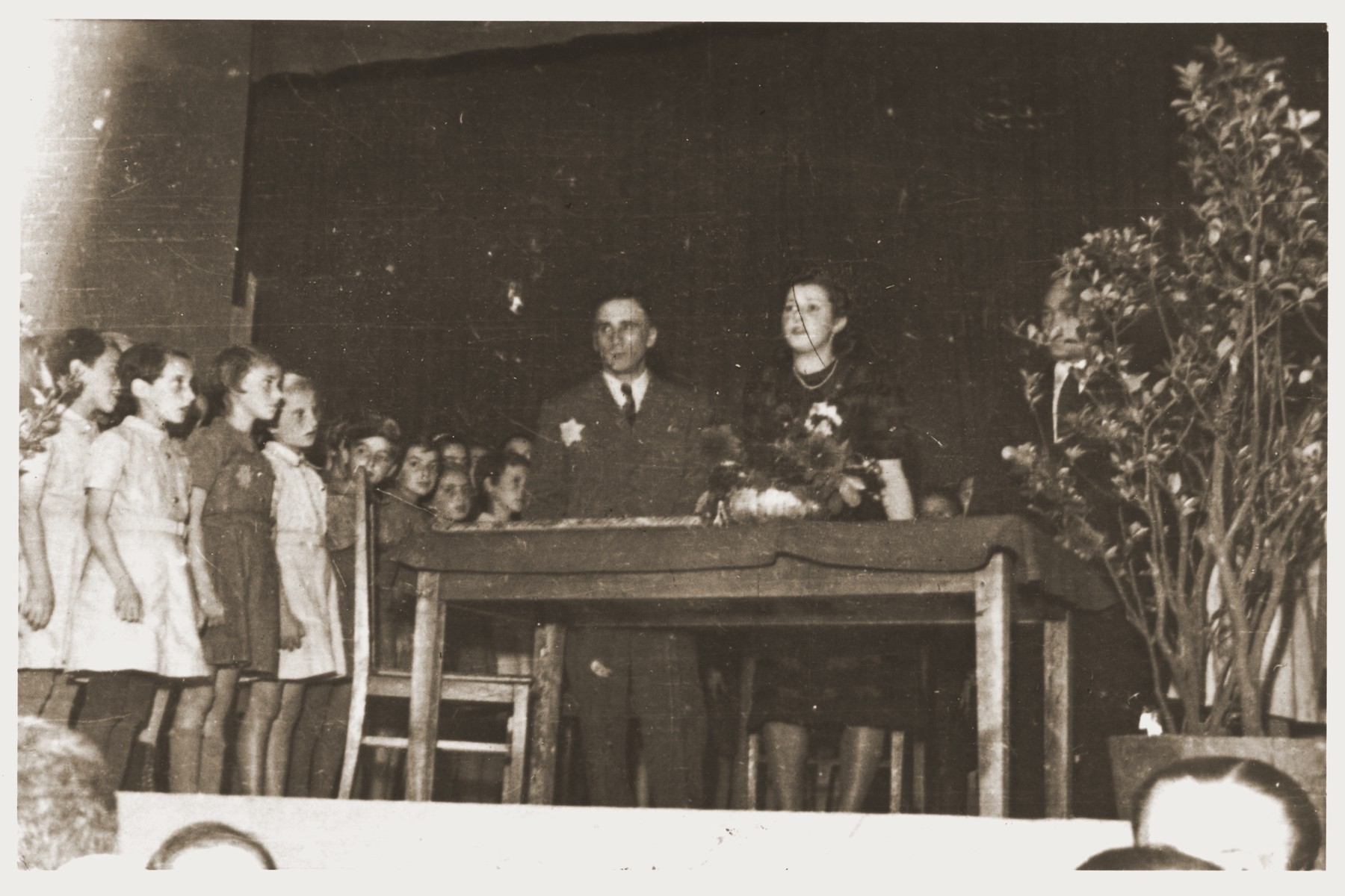 A group of school children are lined up on a stage during a formal presentation in the Lodz ghetto.