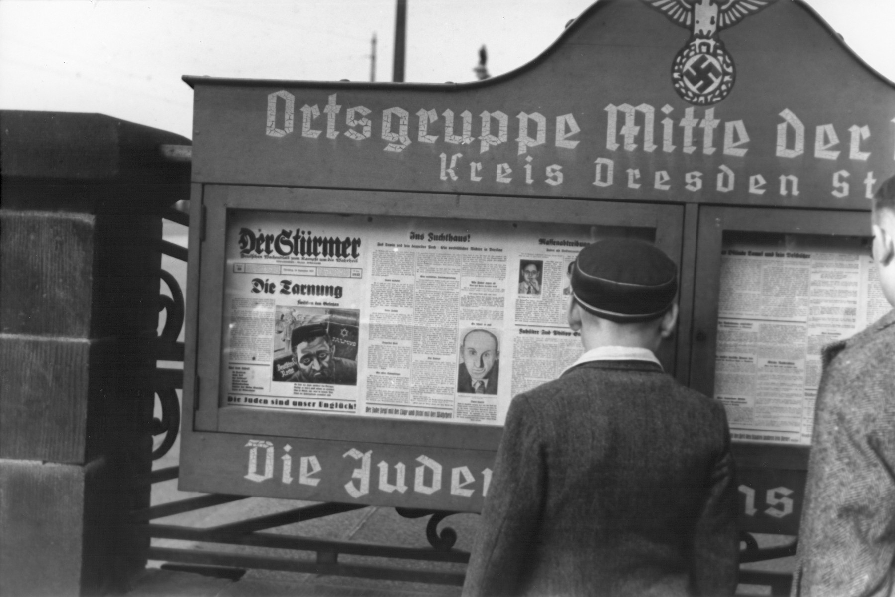 German boys read an issue of the Stuermer newspaper that is posted in a display box at the entrance to a Nazi party headquarters (Ortsgruppe Mitte der NSDAP) in the Dresden region.

The German slogan at the bottom of the display box reads, "The Jews are our misfortune."