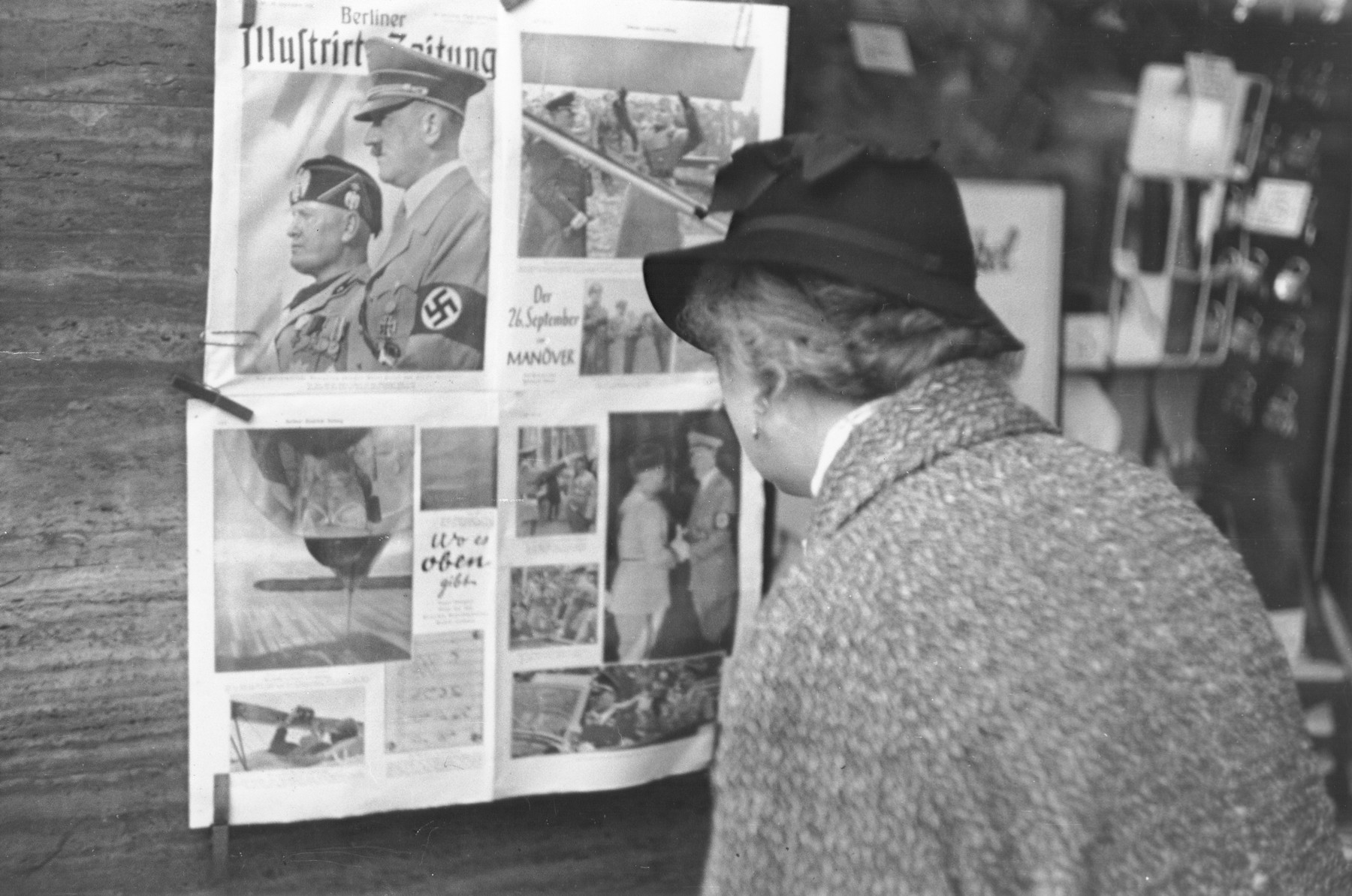 A German woman reads a copy of the Berliner Illustrierte newspaper that has been posted on a wall in Berlin.  It features photographs of Mussolini's official visit to Berlin in September 1937.