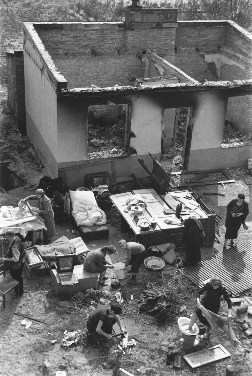 View from above of a Polish family performing their daily chores amidst the remnants of their household furnishings that they have reassembled outside the charred ruins of their home in Warsaw.  

The boy with the hatchet is Albert Turowski, who later became a film actor in postwar Poland.