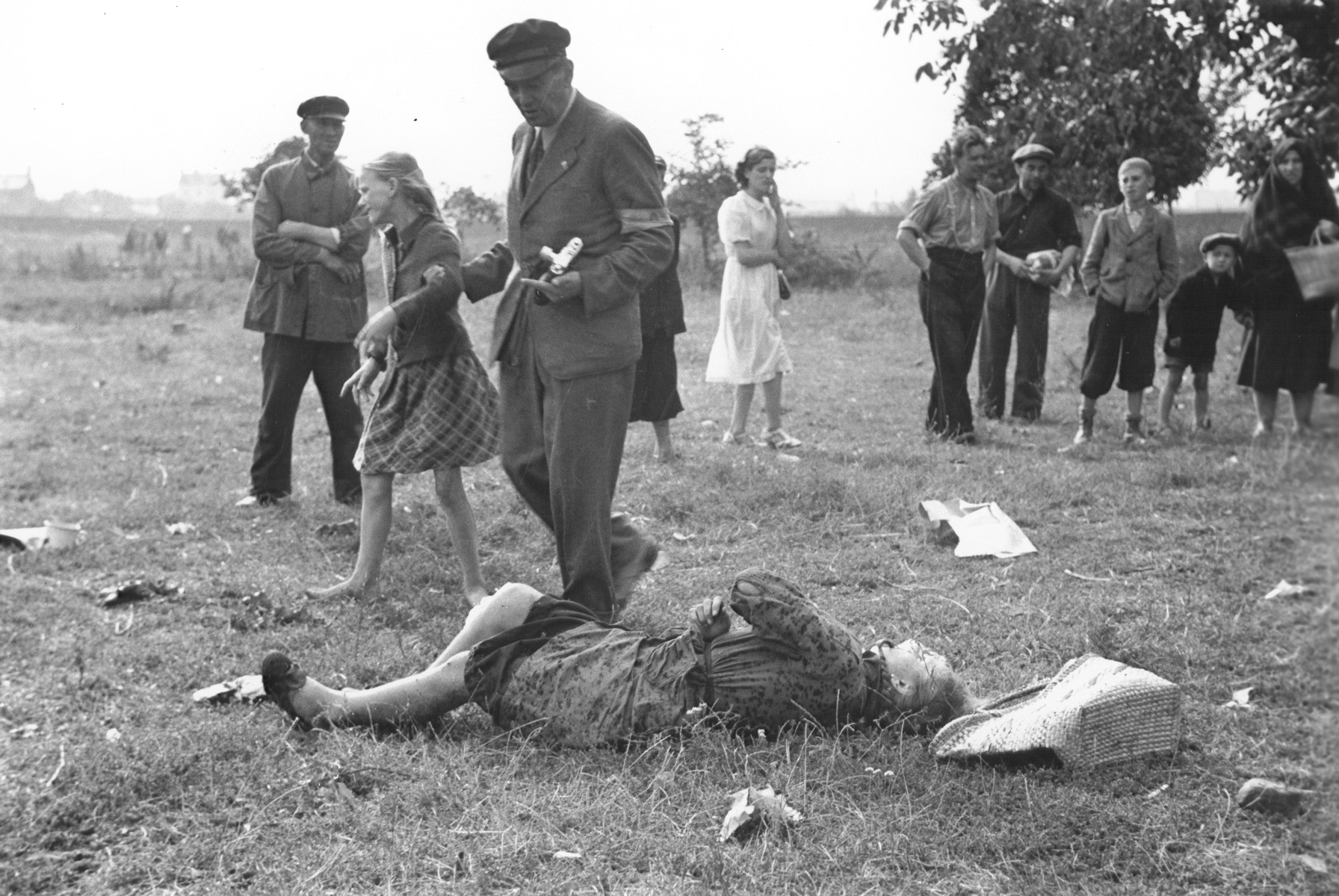 A Polish man wearing an armband and holding a camera leads away a ten-year-old girl named Kazimiera Mika from the body of her older sister, who was killed in a field in Warsaw during a German air raid.

In the words of photographer Julien Bryan, "As we drove by a small field at the edge of town we were just a few minutes too late to witness a tragic event, the most incredible of all.  Seven women had been digging potatoes in a field.  There was no flour in their district, and they were desperate for food.  Suddenly two German planes appeared from nowhere and dropped two bombs only two hundred yards away on a small home.  Two women in the house were killed.  The potato diggers dropped flat upon the ground, hoping to be unnoticed.  After the bombers had gone, the women returned to their work.  They had to have food.

But the Nazi fliers were not satisfied with their work.  In a few minutes they came back and swooped down to within two hundred feet of the ground, this time raking the field with machine-gun fire.  Two of the seven women were killed.  The other five escaped somehow.

While I was photographing the bodies, a little ten-year old girl came running up and stood transfixed by one of the dead.  The woman was her older sister.  The child had never before seen death and couldn't understand why her sister would not speak to her...

The child looked at us in bewilderment.  I threw my arm about her and held her tightly, trying to comfort her.  She cried.  So did I and the two Polish officers who were with me..."  [Source: Bryan, Julien. "Warsaw: 1939 Siege; 1959 Warsaw Revisited." Warsaw, Polonia, 1959, pp.20-21.]