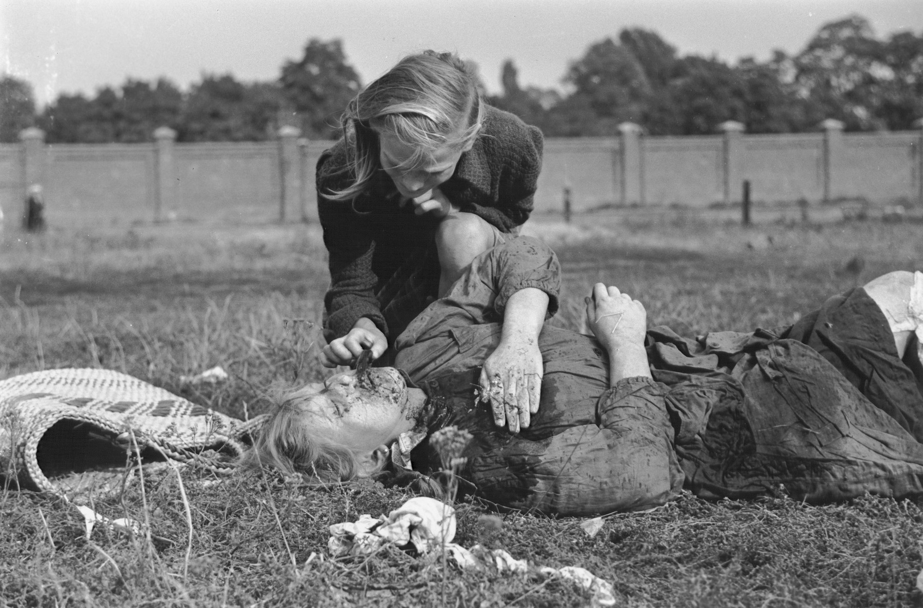 A ten-year-old Polish girl named Kazimiera Mika, mourns the death of her older sister, who was killed in a field in Warsaw during a German air raid.

In the words of photographer Julien Bryan, "As we drove by a small field at the edge of town we were just a few minutes too late to witness a tragic event, the most incredible of all.  Seven women had been digging potatoes in a field.  There was no flour in their district, and they were desperate for food.  Suddenly two German planes appeared from nowhere and dropped two bombs only two hundred yards away on a small home.  Two women in the house were killed.  The potato diggers dropped flat upon the ground, hoping to be unnoticed.  After the bombers had gone, the women returned to their work.  They had to have food.

But the Nazi fliers were not satisfied with their work.  In a few minutes they came back and swooped down to within two hundred feet of the ground, this time raking the field with machine-gun fire.  Two of the seven women were killed.  The other five escaped somehow.

While I was photographing the bodies, a little ten-year old girl came running up and stood transfixed by one of the dead.  The woman was her older sister.  The child had never before seen death and couldn't understand why her sister would not speak to her...

The child looked at us in bewilderment.  I threw my arm about her and held her tightly, trying to comfort her.  She cried.  So did I and the two Polish officers who were with me..."  [Source: Bryan, Julien. "Warsaw: 1939 Siege; 1959 Warsaw Revisited." Warsaw, Polonia, 1959, pp.20-21.]