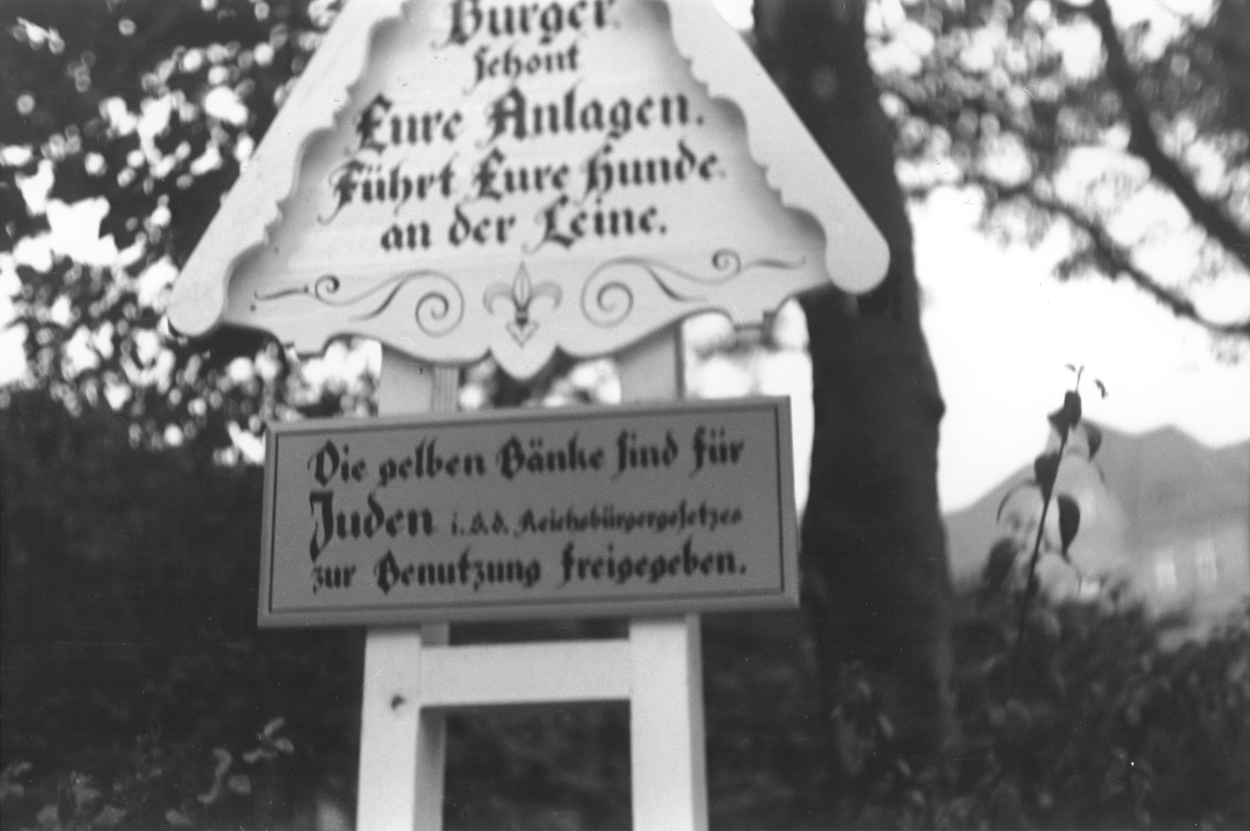 A decorative sign in a public park in the Oliviaplatz reads: "Citizens protect your public spaces.  Keep your dogs on a leash.  The yellow benches are for Jews (in accordance with the Reich's law) for their free use."