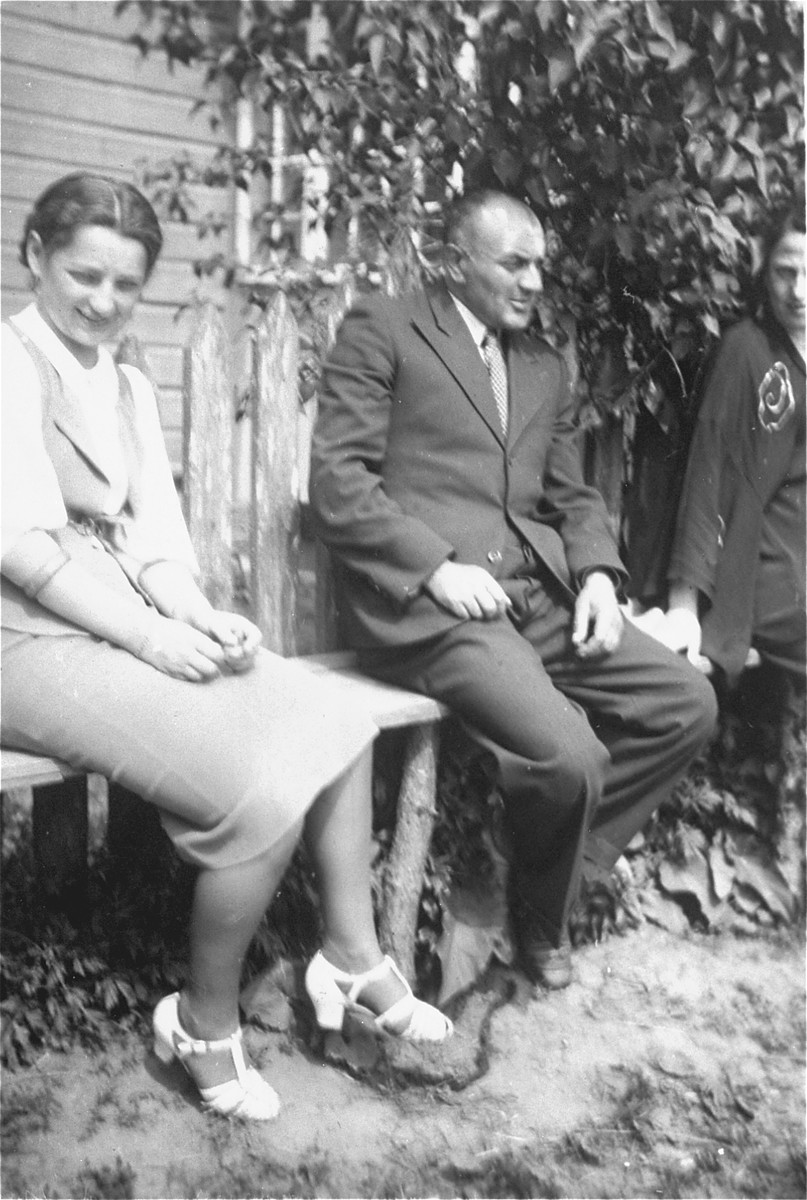 A Jewish man and woman from Sejny sit outside a wooden house.

The man is Peretz (exact name unknown); the brother-in-law of Zelig Szczupacki.  Peretz owned an iron-goods store.  His father in-law Avram was a blacksmith.