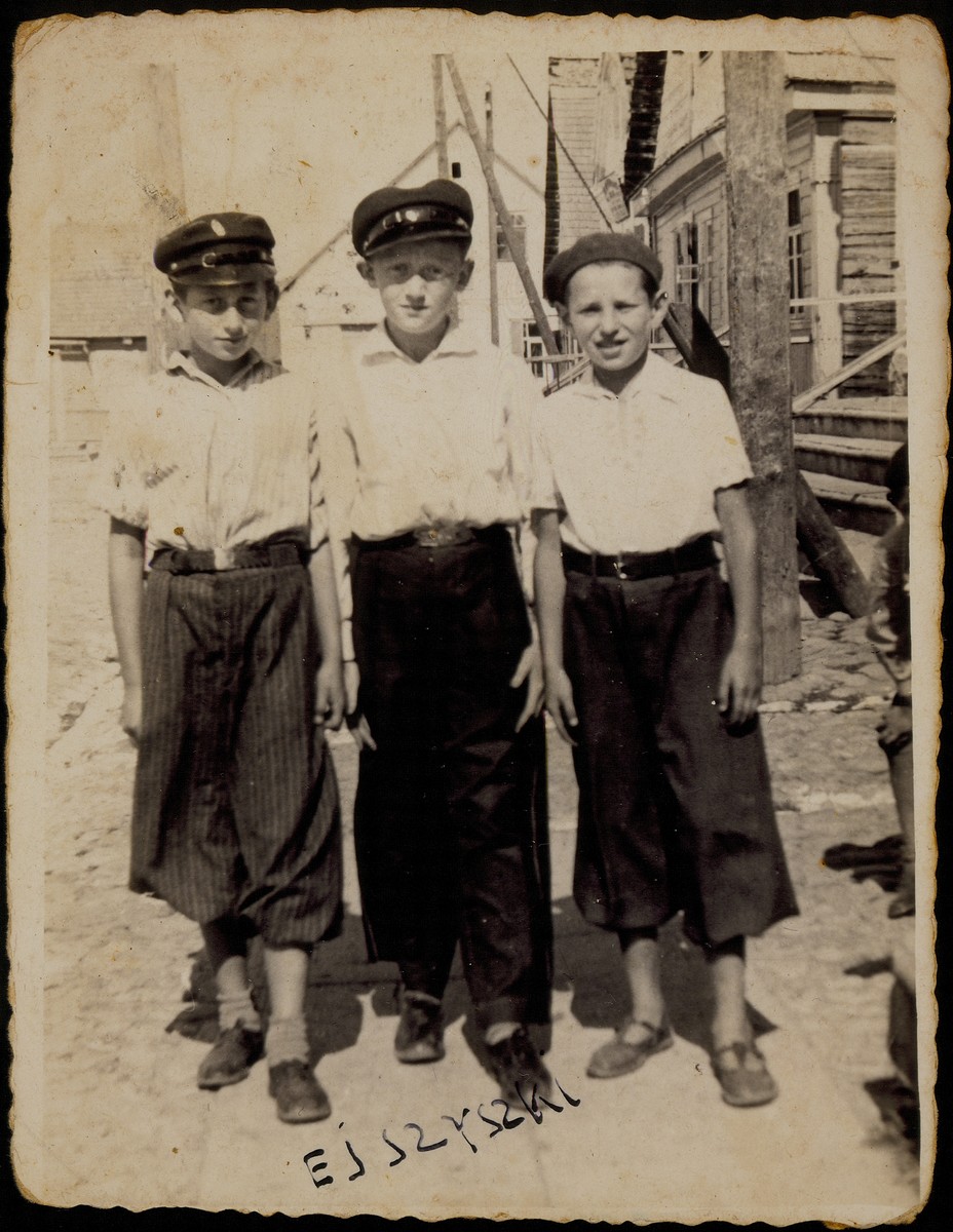 Three best friends stand in the market square near the house of Alte Katz.

(left to right): Avigdor Katz, Moshe Bastunski, and Avraham Botwinik.

Avigdor and Moshe were murdered by the Germans during the September 1941 mass shooting action. Avraham survived as a partisan and emigrated to the United States.