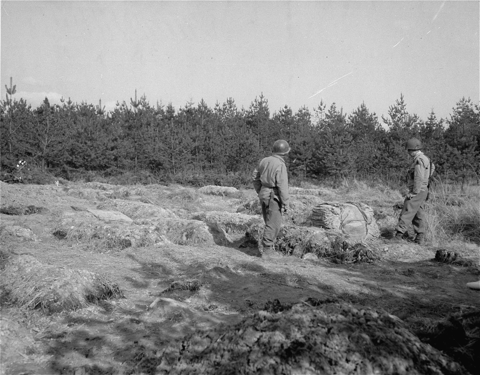 Two U.S. soldiers with the 9th Armored Division stand in the middle of a field of graves, near the Flossenbuerg concentration camp.