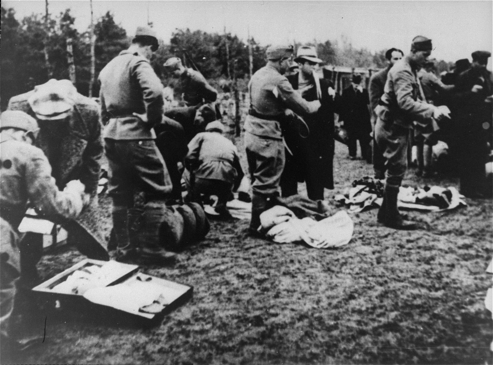 Ustasa guards confiscate the possessions of newly arrived prisoners in the Jasenovac concentration camp.

Andor Willer is pictured being frisked in the lcenter oreground in the light colored hat and dark overcoat with a document in his mouth.