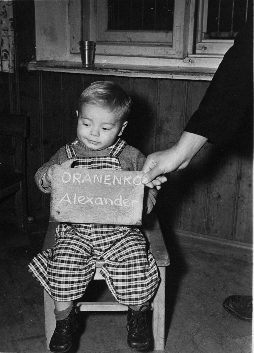 Alexander Dranenko holds a name card intended to help any of his surviving family members locate him at the Kloster Indersdorf DP camp.  This photograph was published in newspapers to facilitate reuniting the family.