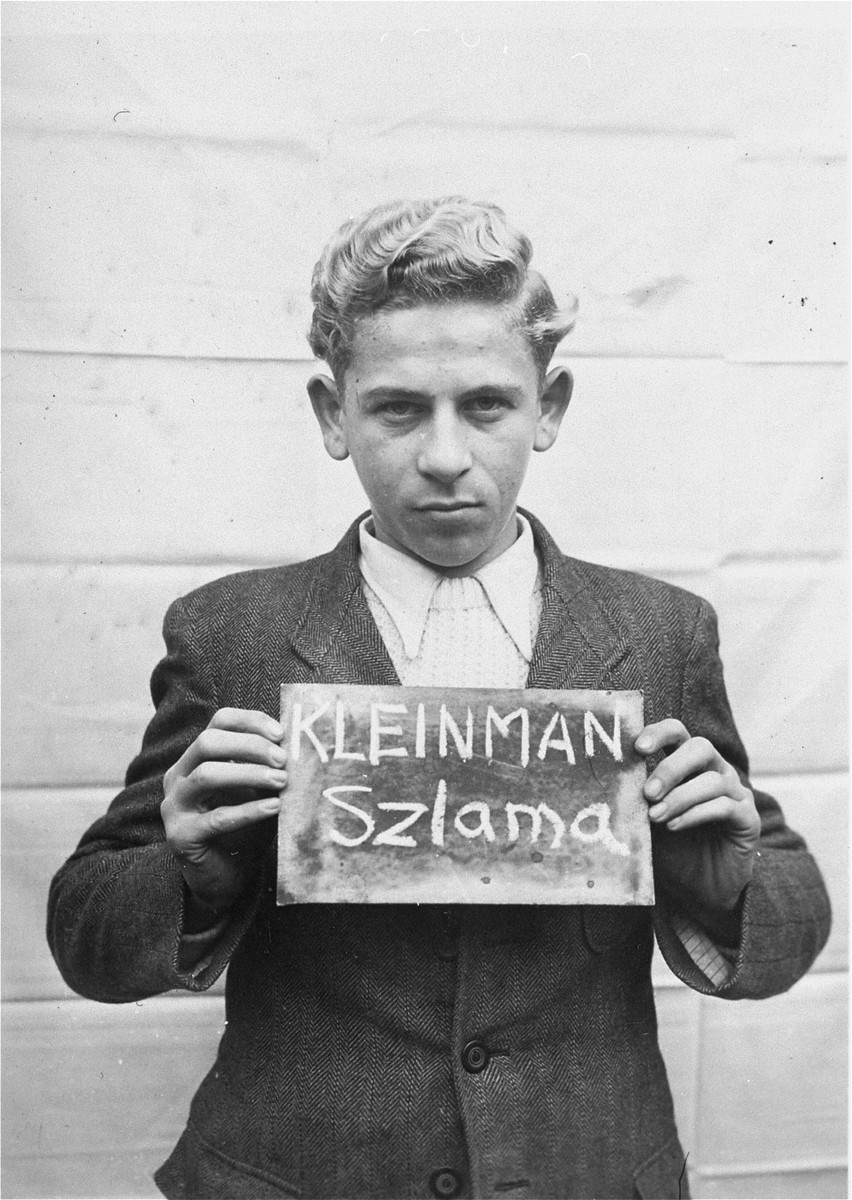 Szlama Kleinman holds a name card intended to help any of his surviving family members locate him at the Kloster Indersdorf DP camp.  This photograph was published in newspapers to facilitate reuniting the family.