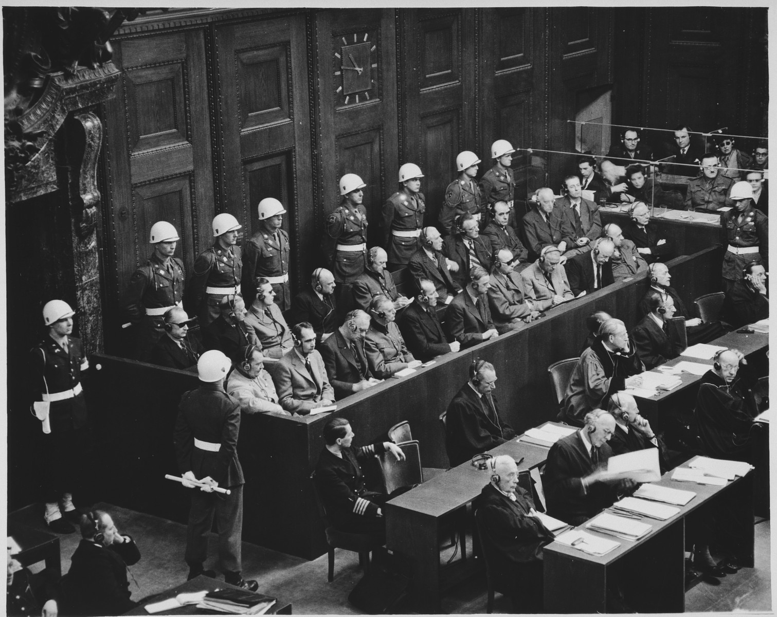 View of the defendants dock at the International Military Tribunal trial of war criminals at Nuremberg.

Pictured in the front row from left to right are: Goering, Hess, Ribbentrop, Keitel, Kaltenburnner, Rosenberg, Frank, Frick, Streicher, Funk and Schacht.  In the second row are Doenitz, Raeder, Schirach, Saukel, Jodl, Papen, Seyss-Inquart, Speer, von Neurath and Fritsche.  Sitting in front of them are their defense counsel.  The naval officer sitting among the lawyers is Dr. Otto Kranzbuehler, the defense counsel for Karl Doenitz, who was given a temporary release from the POW camp when Doenitz requested him to be his lawyer.  At the bottom left corner is General R. A. Rudenko, the chief Soviet prosecutor.