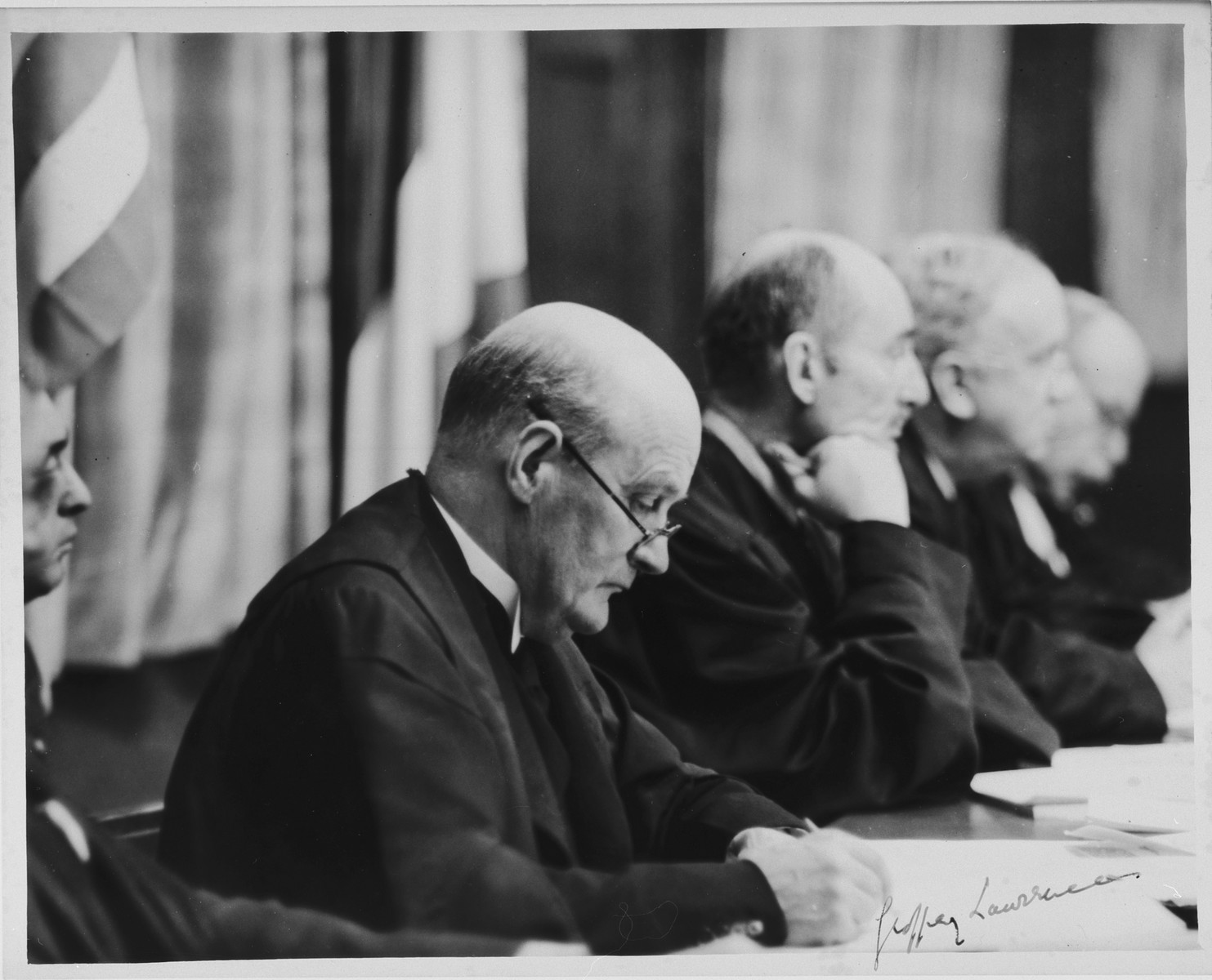 Presiding judge, Sir Geoffrey Lawrence, KC, sits on the bench during a session of the International Military Tribunal trial of war criminals at Nuremberg.

Visible in the background are Judge Francis Biddle, Justice John L. Parker and Justice Donnedieu de Varbes.