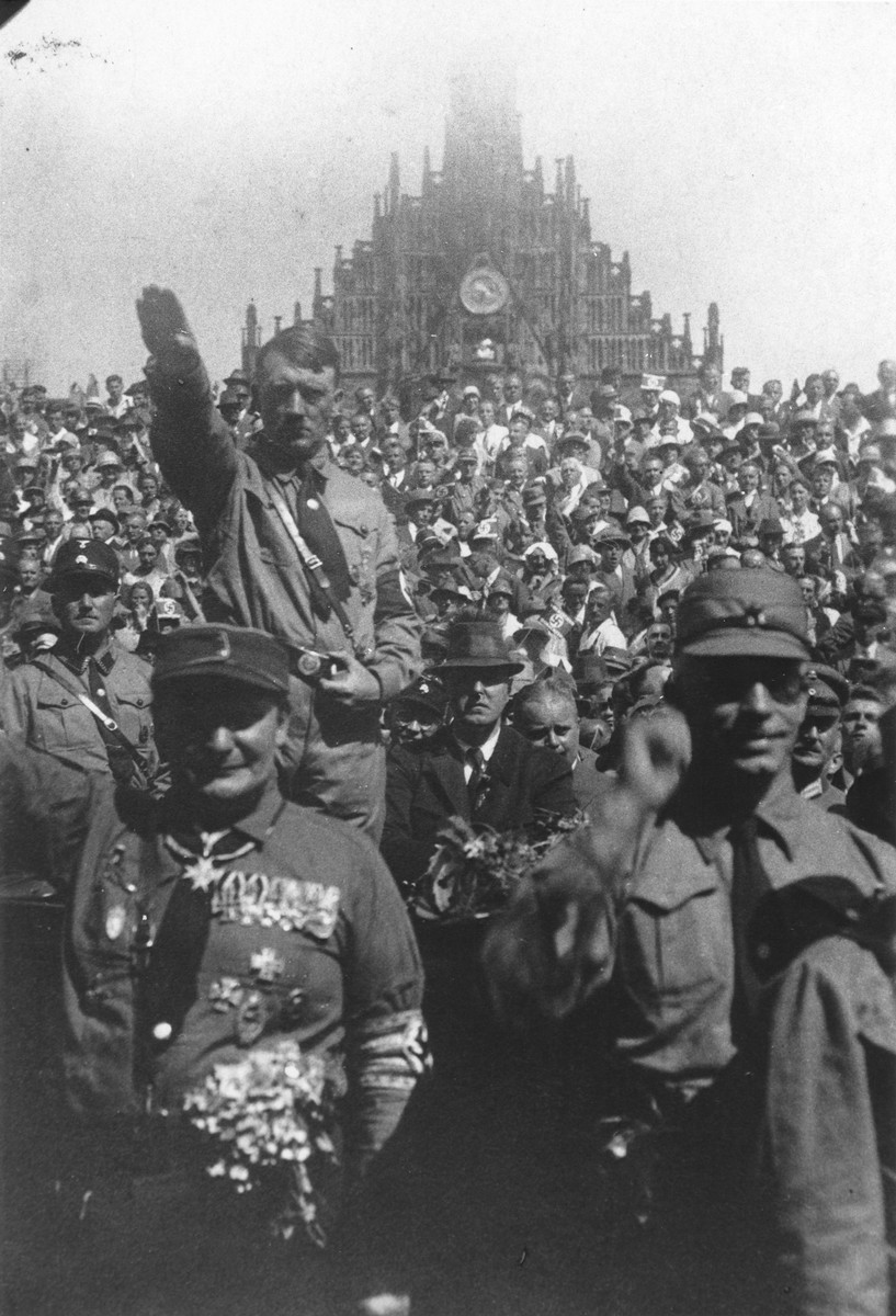 Standing amidst a large crowd, Adolf Hitler gives the Nazi salute during a Reichsparteitag (Reich Party Day) rally. 

In front of him is Hermann Goering.