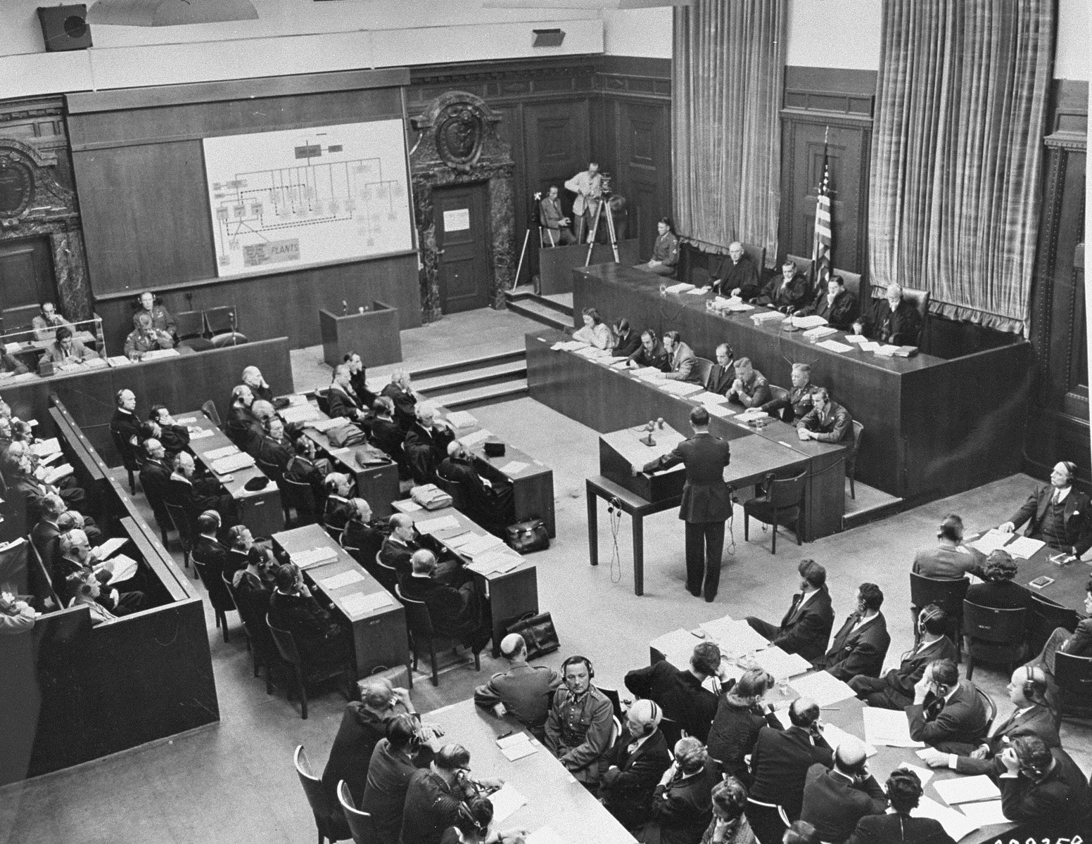 US Chief of Counsel Brigadier General Telford Taylor (standing in center) opens the prosecution's case in front of the Military Tribunal VI (upper right) at the I.G. Farben Trial.