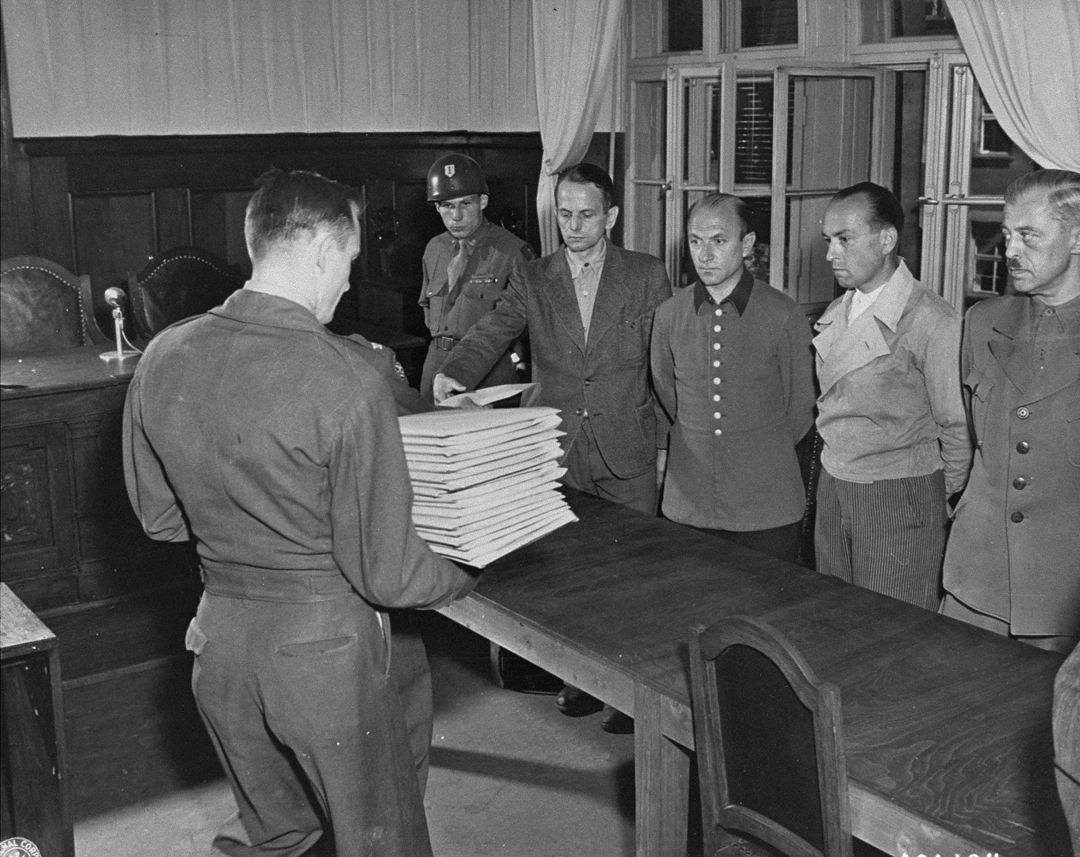 Defendant Otto Ohlendorf (left) receives his indictment from Col. C.W. Mays, Marshal of the Military Tribunal, before the Einsatzgruppen Trial.  The other defendants (left to right) are, Heinz Jost, Erich Naumann, and Erwin Schulz.