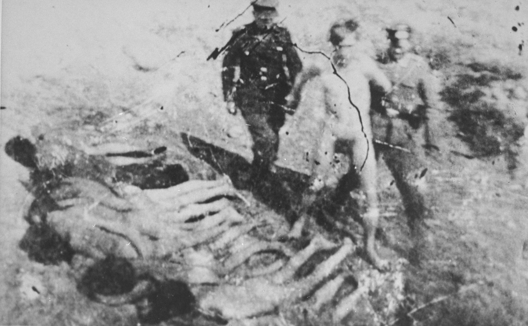 A naked prisoner is led to an execution site, possbily Ponary, where others either have been shot already or forced to lie face down prior to being shot.