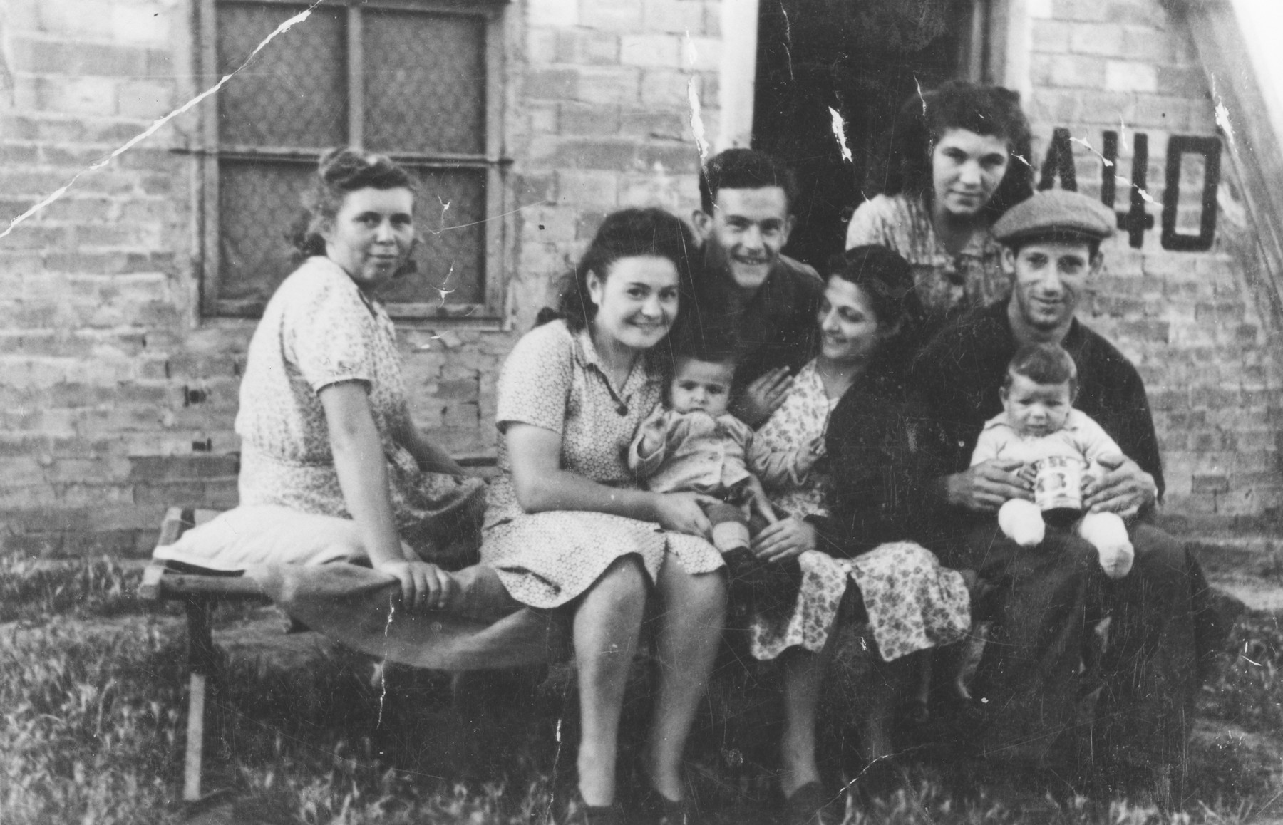 Group portrait of Jewish DPs outside a barracks in the Bari displaced persons camp.

Among those pictured are Izidor and Tauba Schachter with their baby Miriam Schachter (now Enright), on the far right; and Etta Gipsman (far left).  Etta  is wearing a dress made from fabric sent by relatives in America.