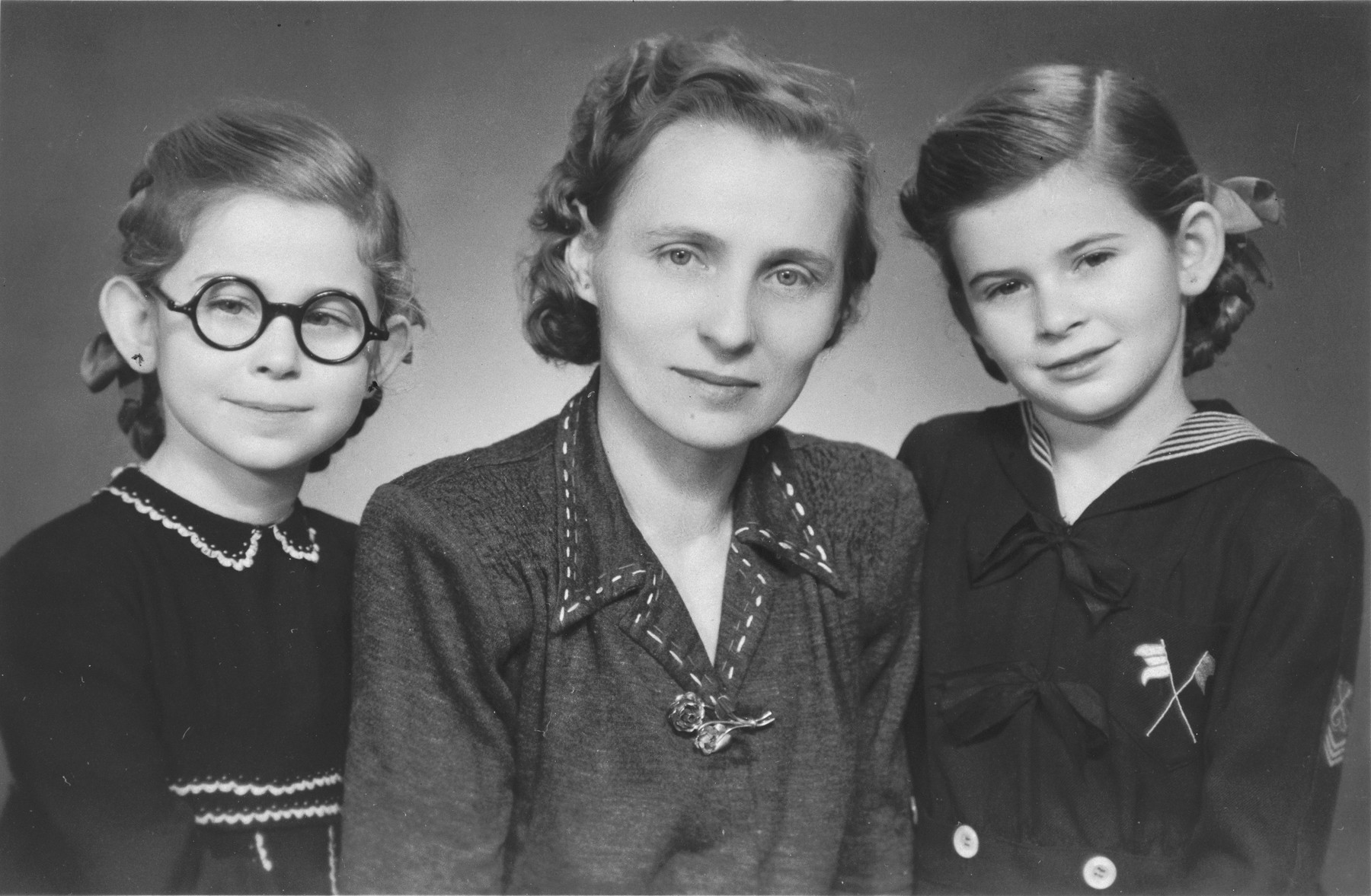 Studio portrait of two Jewish sisters with their rescuer after the war.

Pictured are Renate (right) and Sylvia Schonberg (left) with their nanny and rescuer, Frantiska Prva.