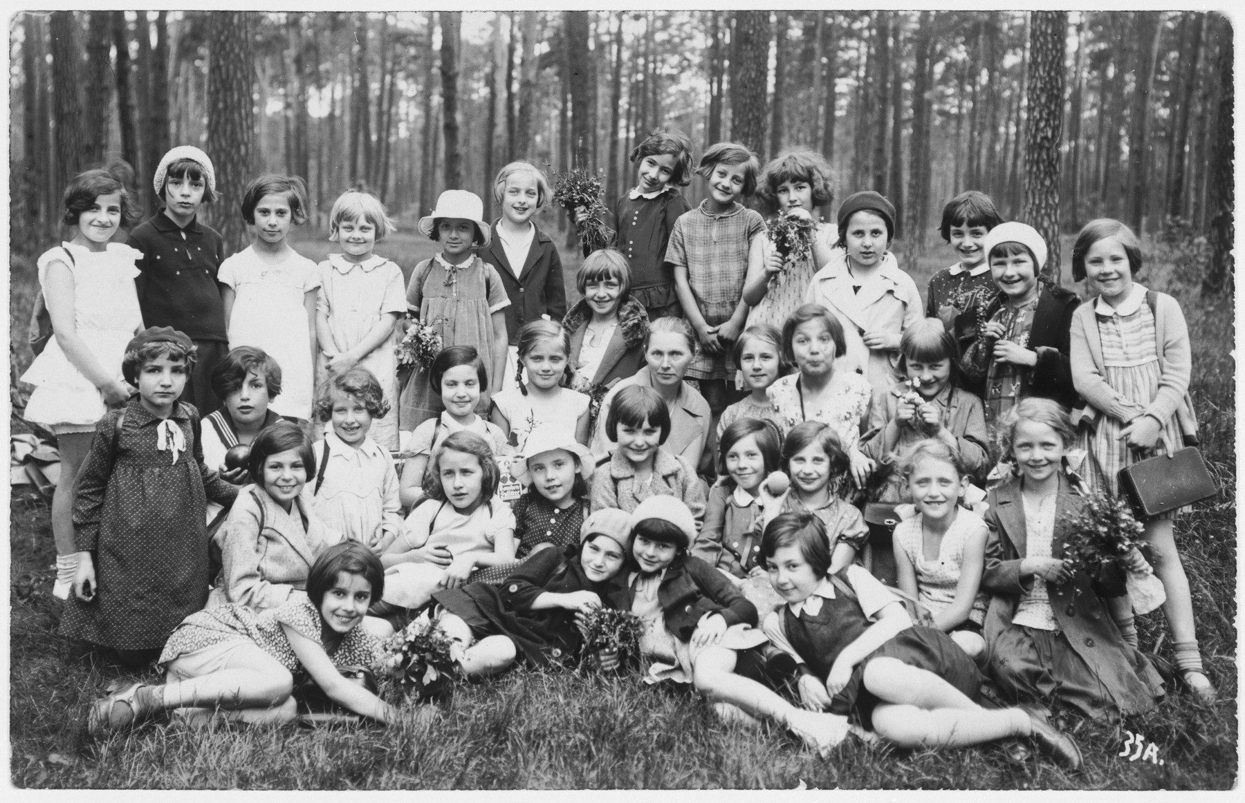 Group portrait of girls, about half of whom are Jewish, from the Hoenstaofen Strasse school, taken during a class outing in a wooded park.

Among those pictured is Ruth Cohn.