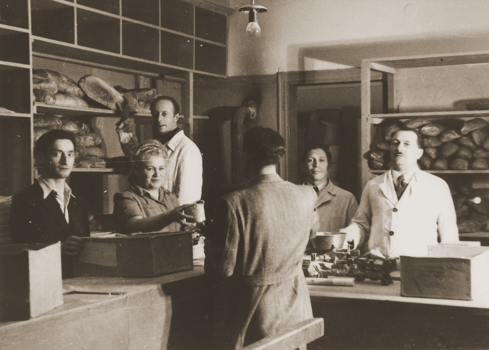 Moses Kornberg (left) and the staff of the Stuttgart DP camp commissary distribute food to one camp resident.

Also among those pictured is Shamai (Sam Greenberg).

One image from the Stuttgart Jewish DP camp album entitled, "Jidiszer D.P. Center UNRRA--P.C.IRO in Stuttgart," compiled and photographed by Alexander Fiedel and dedicated to Moses Kornberg, head of the commissary.
