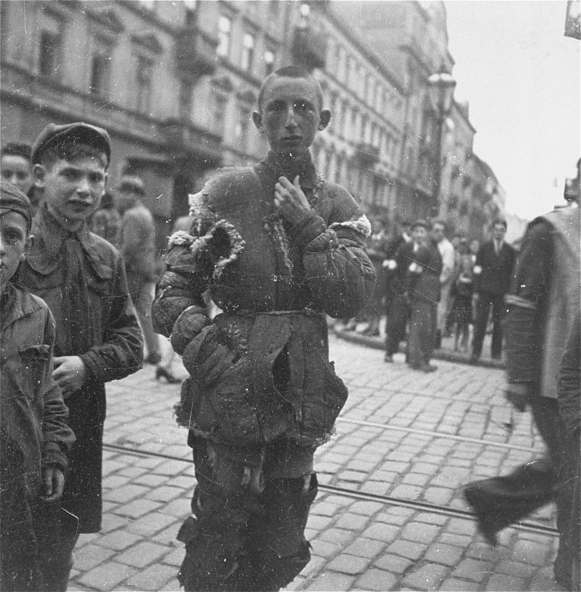 A destitute youth in the Warsaw ghetto.  

Joest's original caption reads: "This youth had a jacket made entirely out of scraps that were stitched together and which had again split in many places.  He had it good in comparison with those children in thin jackets who were not wearing even one shoe."