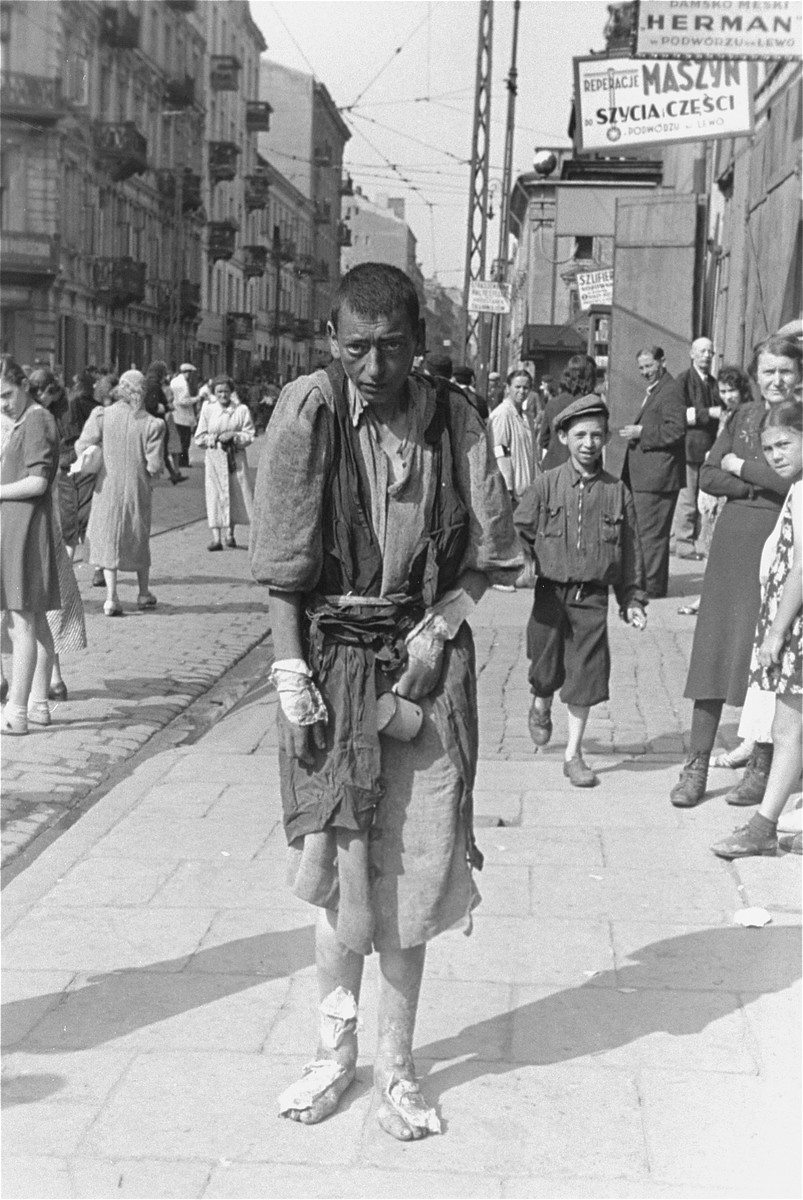 A bandaged, destitute Jewish youth walks along a street in the Warsaw ghetto.