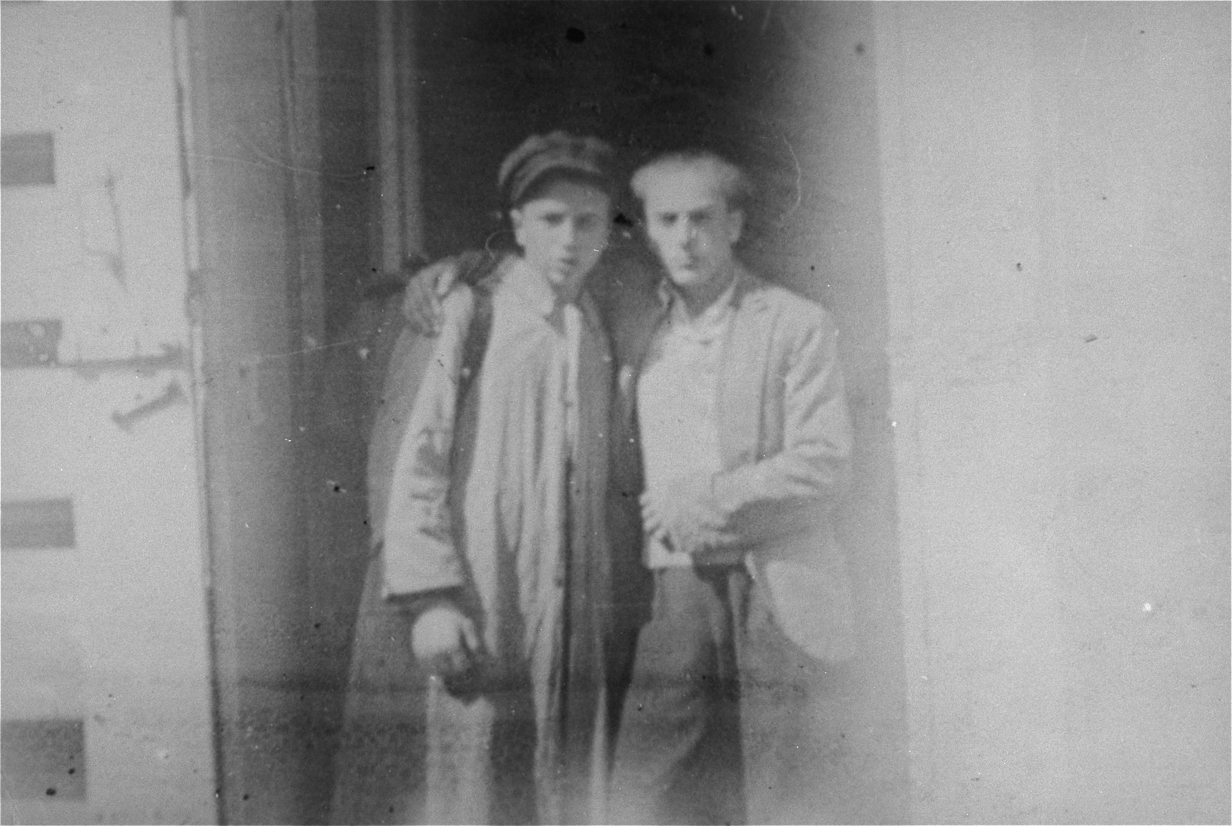 Two Jewish youth who are posing as Poles stand outside in a doorway on the Aryan side of Warsaw.

Pictured are Ignacy (Byczek) Milchberg (left) and Izaak (Zbyszek) Grynberg (right), two of a group of 20 Jewish children who were living in hiding on the Aryan side of Warsaw and supporting themselves by selling cigarettes in Three Crosses Square.