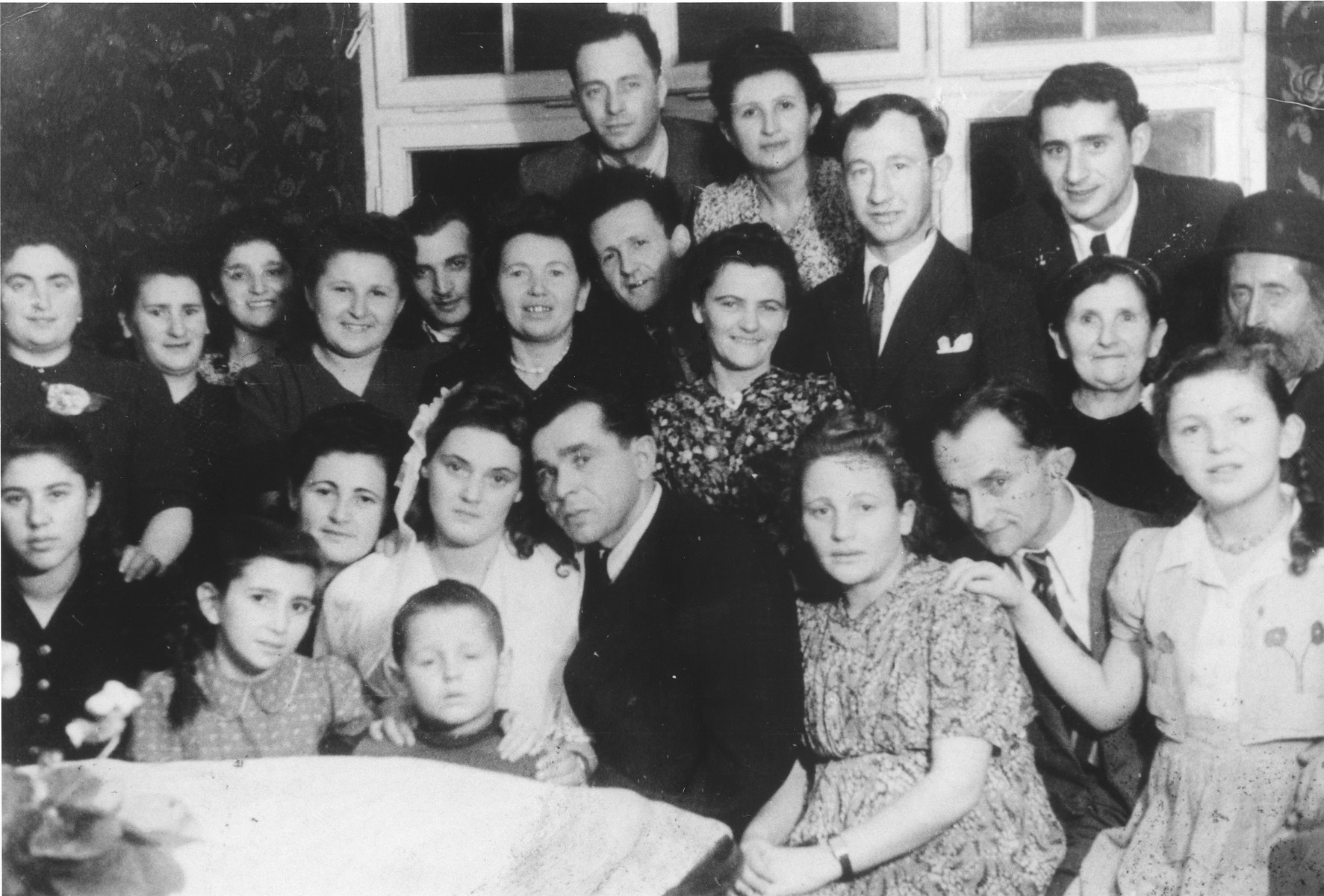 Group portrait of family and friends at the first wedding in the Ulm displaced persons camp. The bride and groom are Dzunia and Joe (Yitchak) (Itche) Storch. 

Also pictured from right to left n the front row are: Lila Rajs, Meyer Fenig and Bina (Rajs) Fenig.  Chuma (Rajs) Fruchter is seated next to the bride on the left.  Directly behind the bride is Chaja Rajs.  To the right of Chaja are Hershel Rajs and Roshi (Rajs) Binder.  Behind them are Moishe Binder and Moishe Fruchter.
