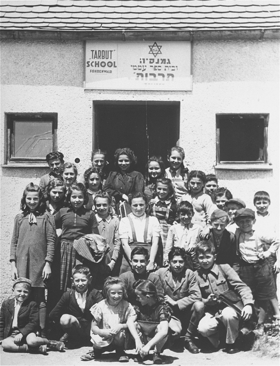 Group portrait of students at the Tarbut school in the Foehrenwald displaced persons camp.   

Among those pictured are:  Abraham Burshtain (Bursztyn) (bottom row, far left). Roman Haar (bottom row, far right); Chaya Libstug (third row, third from left) in braids; Pesa Balter (second row from the top, third from the right) and Chaim Swidler (second row from bottom, second from the right).  Paula Lebovics is pictured  in the center back, wearing a plaid jumper.  Ludka Herzig (later Lucille Lebowitz) is pictured in the first standing row, second from the left, wearing a plaid skirt.  Also pictured is Bezalel Rotman..