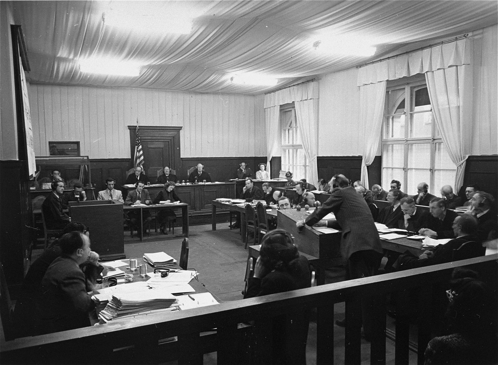 The proceedings of the RuSHA Trial in Courtroom #6 in the Palace of Justice.  

In the back sits Military Tribunal I, to the right is the defendants' dock, and in front are the lawyers.  Sitting below the middle judge of the Tribunal is Vivien Putty Spitz, a court reporterr.