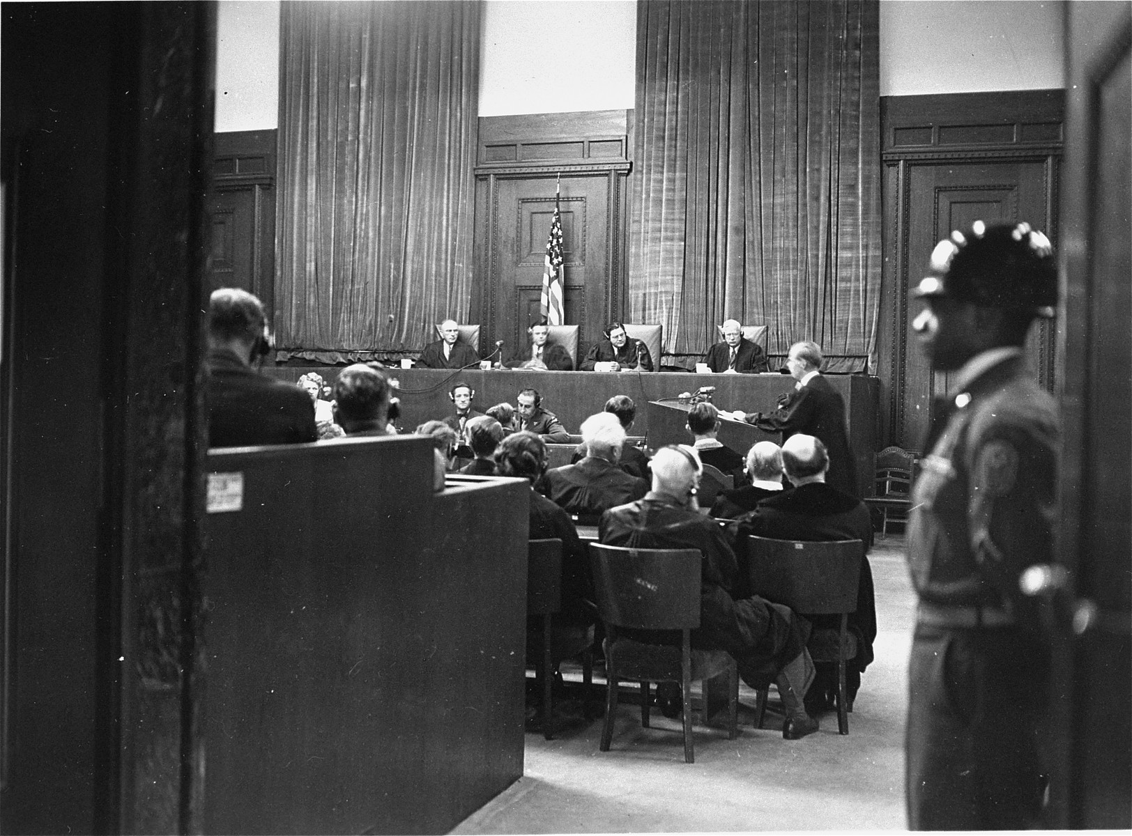 An American soldier guards the main entrance to the courtroom during the I.G. Farben Trial.  In the back sits the Military Tribunal VI.