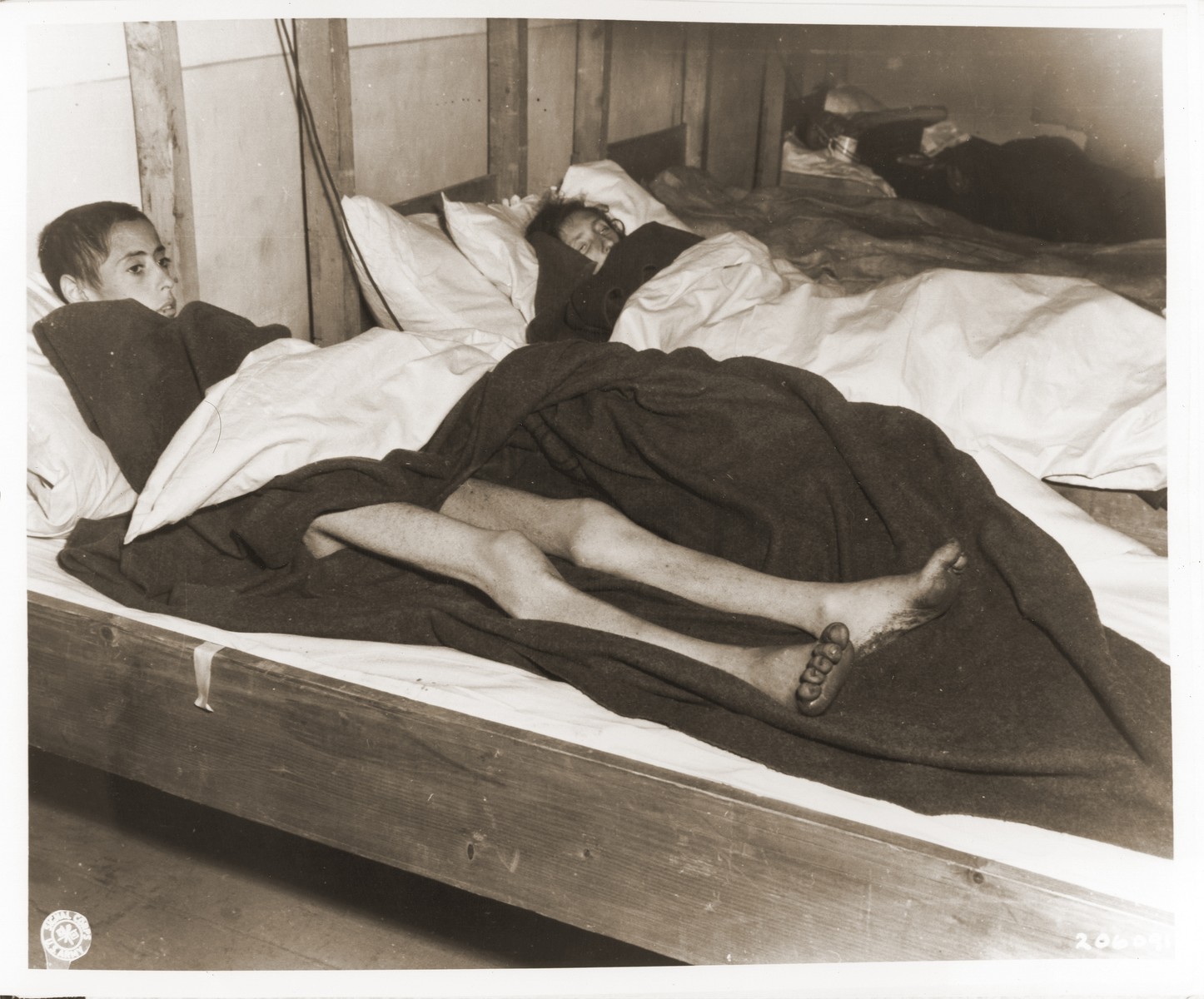 Two emaciated female Jewish survivors of a death march lie in an American military field hospital in Volary, Czechoslovakia.

Pictured on the left is seventeen-year-old Nadzi Rypsztajn.

The original caption reads "This girl, only seventeen years old, was forced to march 18 miles a day for 30 days on one bowl of soup a day.  The 5th Infantry Division of the U.S. Third Army found 150 in the same condition when they entered Volary, Czechoslovakia."