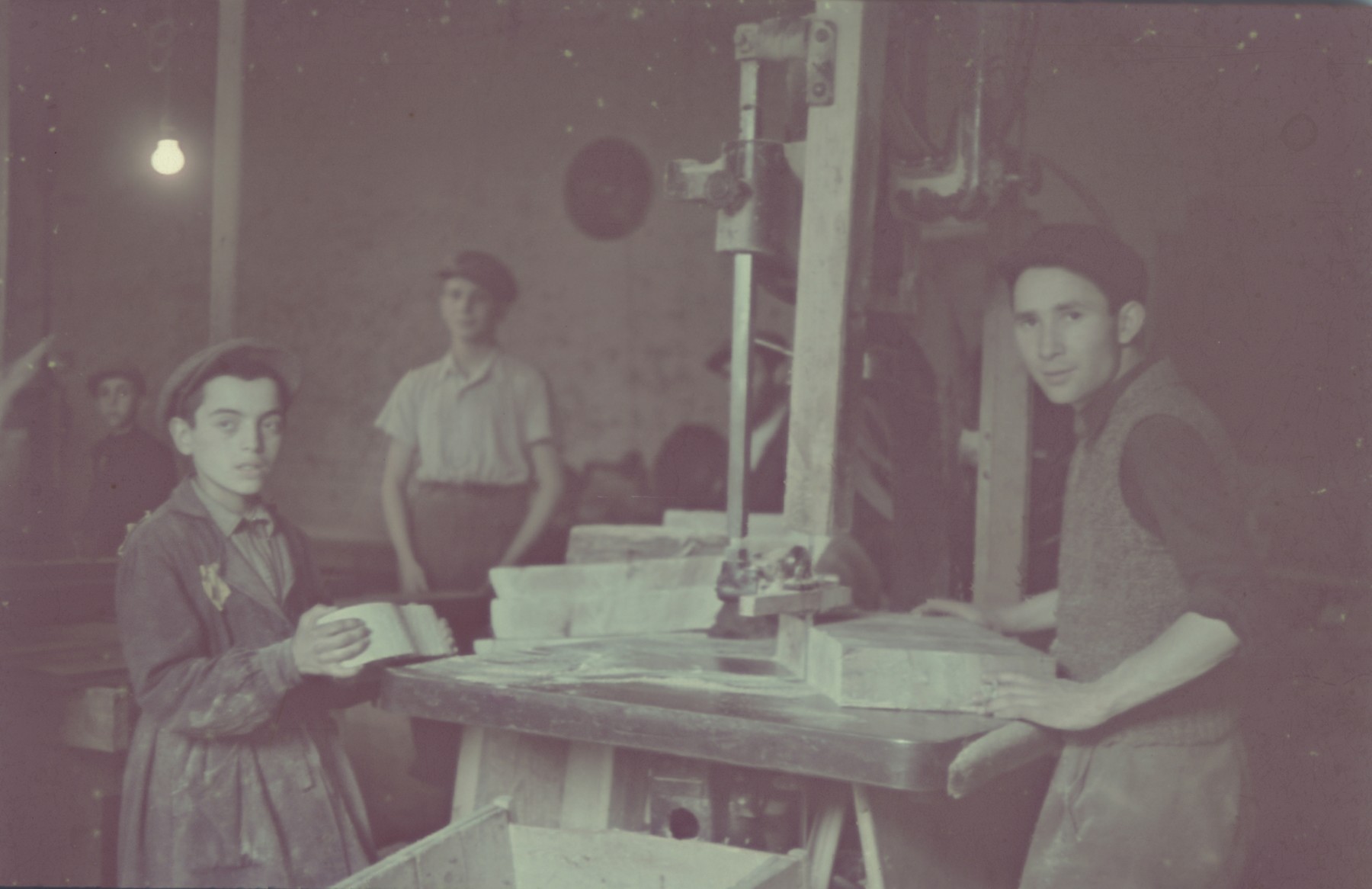 Jewish youth cut blocks of wood in the furniture workshop in the Lodz ghetto.

Standing second from the left is Yerszyk Hellmer.  Daniel Geslewitz identified himself as one of the young men pictured.

Original German caption: "Litzmannstadt Getto, Moebelfabrik" (furniture factory), #11.