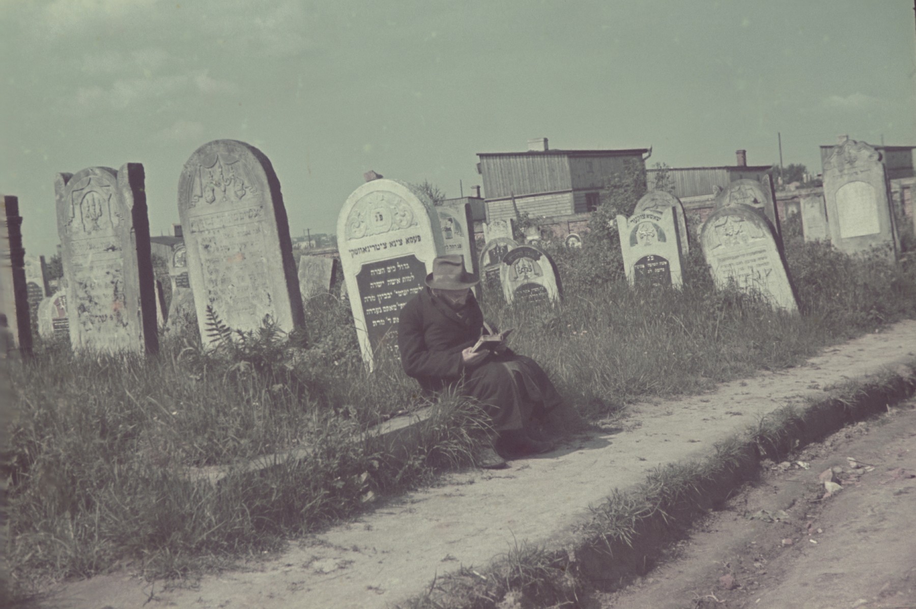 A bearded Jew reads a book next to a tombstone in the Lodz ghetto cemetery.