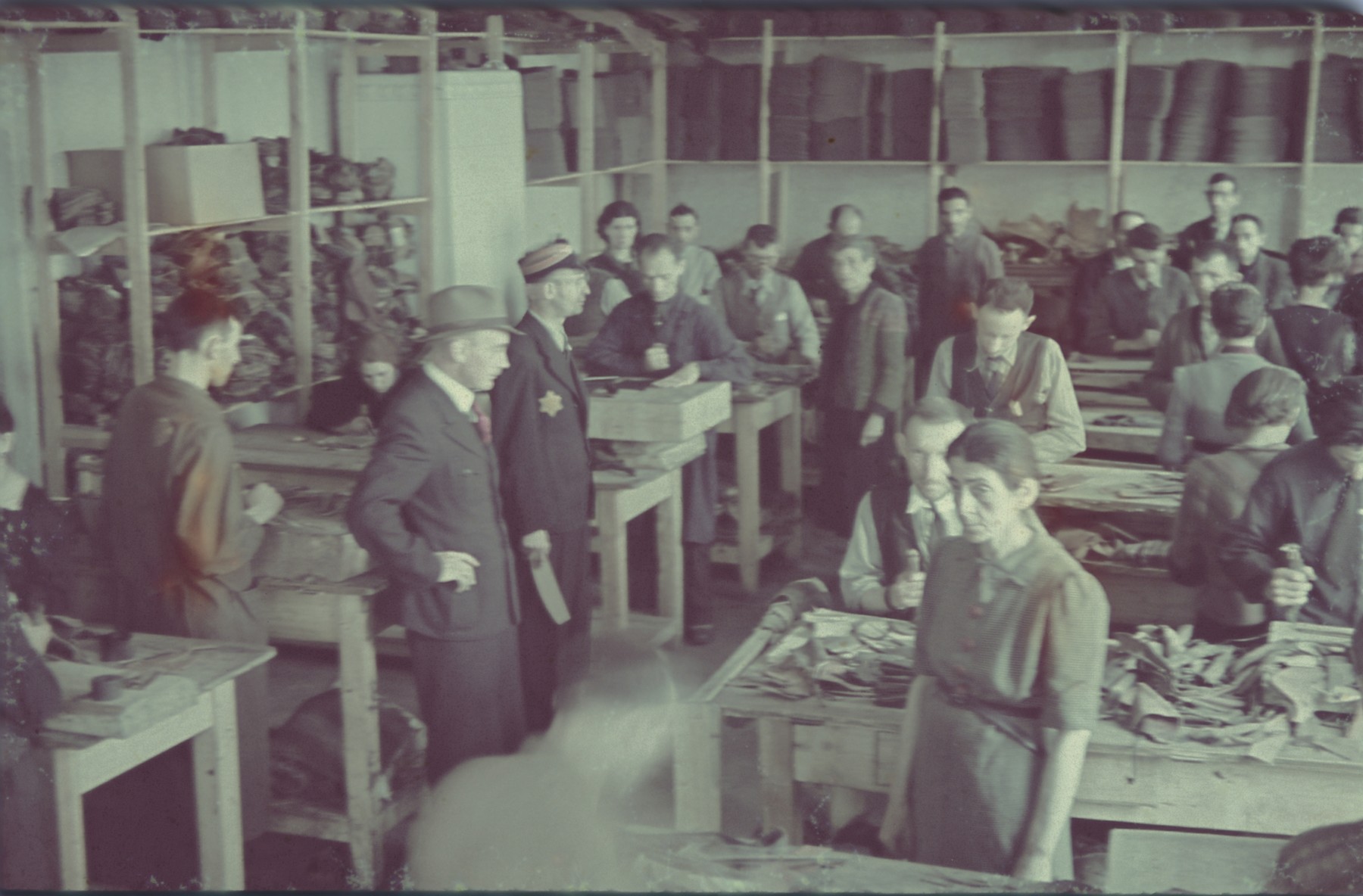 Workers at the saddle-making workshop stand next to their work tables in the Lodz ghetto.

Original German caption: "Litzmannstadt-Get, Sattlerei" (saddlery).