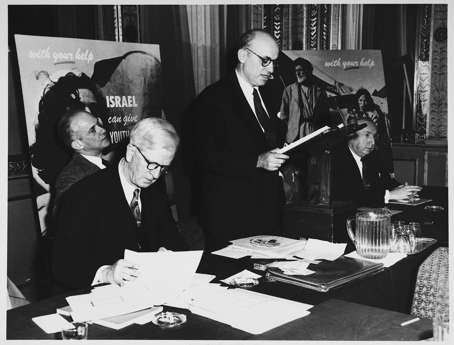 James G. McDonald (seated, left), Chairman of the Advisory Council, Development Corporation for Israel, looks through his papers while attending a conference about fundraising for the State of Israel.